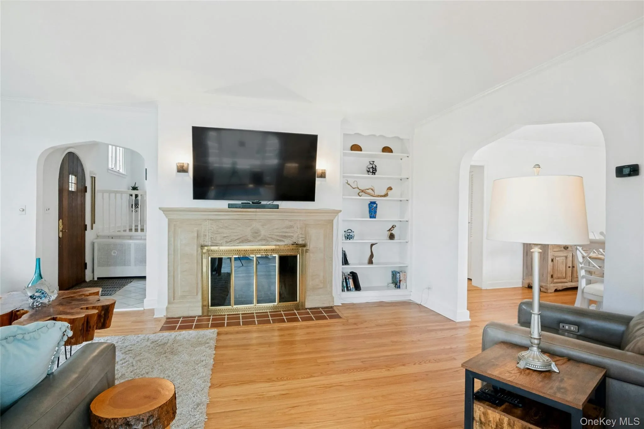 Living area featuring hardwood flooring, a decorative fireplace with a stone mantel, recessed built-in shelving, and arched doorways Living area featuring hardwood flooring, a decorative fireplace with a stone mantel, recessed built-in shelving, and arched doorways
