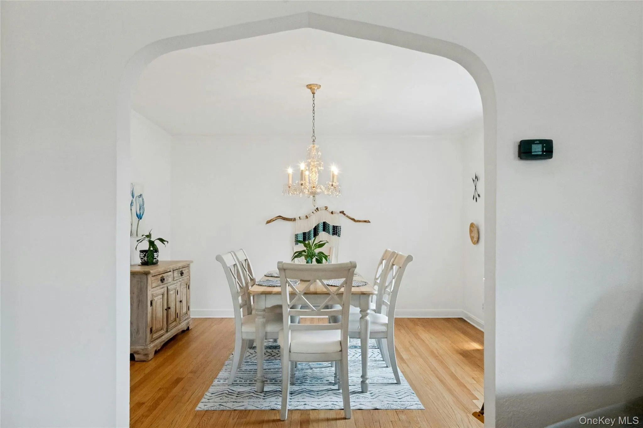 Dining area featuring an arched entryway, wood-finish flooring, a chandelier-style light fixture, and white wall finishes Dining area featuring an arched entryway, wood-finish flooring, a chandelier-style light fixture, and white wall finishes