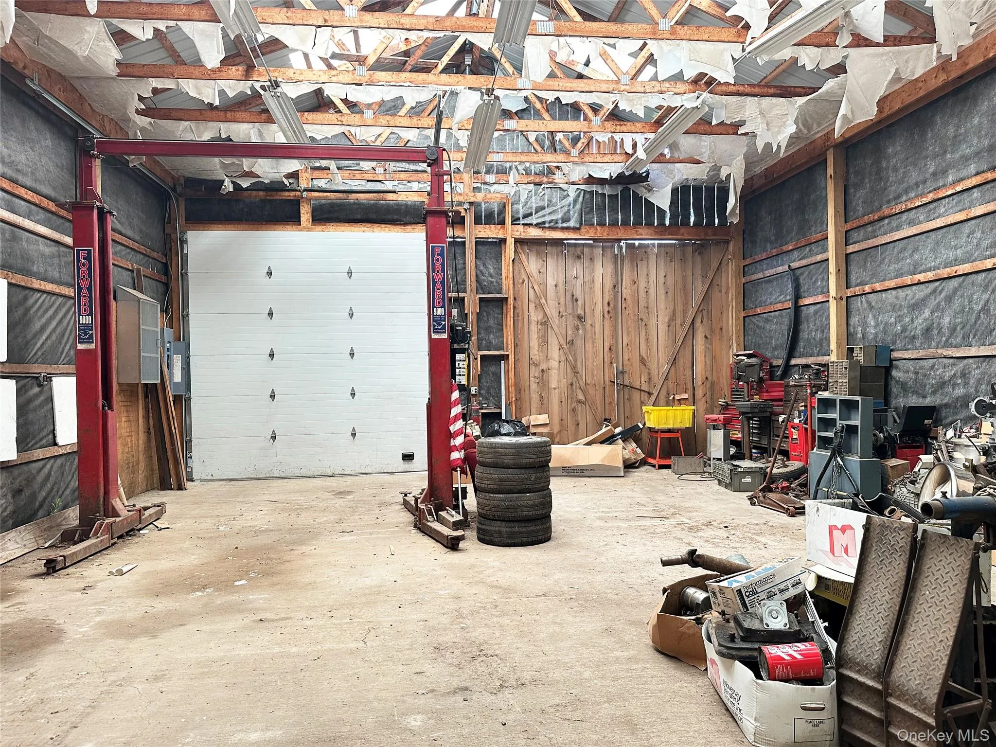 Additional oversized garage interior featuring vehicle lift, soaring ceilings, and substantial open-span workspace ideal for collectors, trades, or recreational storage. Additional oversized garage interior featuring vehicle lift, soaring ceilings, and substantial open-span workspace ideal for collectors, trades, or recreational storage.