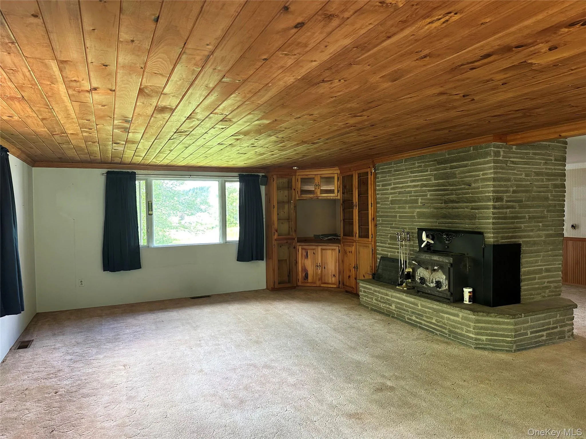 Spacious living room with original 1960s character, wood-paneled ceiling, built-in cabinetry, and fireplace designed for both heating and cooking. Spacious living room with original 1960s character, wood-paneled ceiling, built-in cabinetry, and fireplace designed for both heating and cooking.