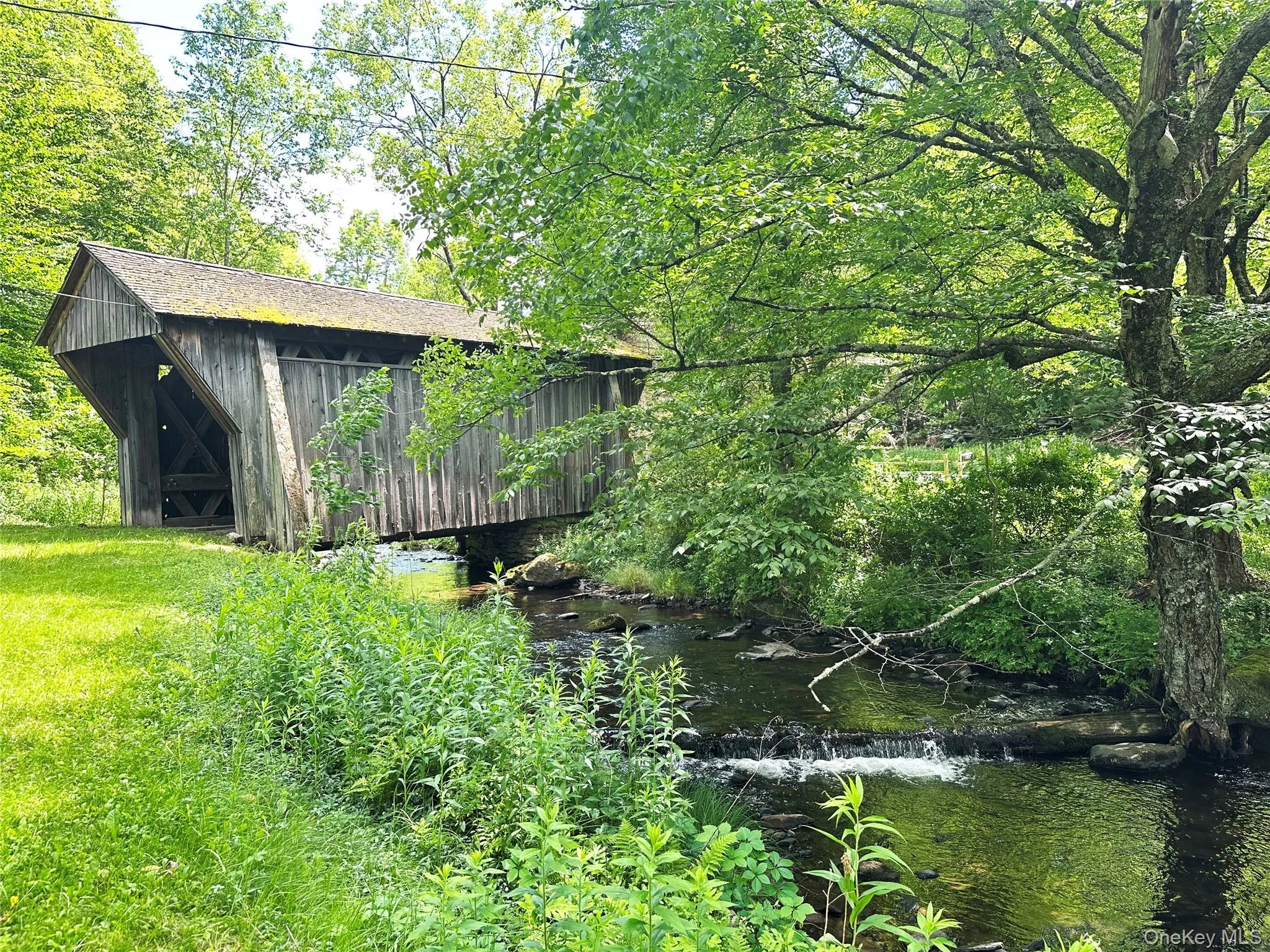 Side view of the historic covered bridge spanning Trout Brook, surrounded by lush greenery and scenic Catskills landscape. Side view of the historic covered bridge spanning Trout Brook, surrounded by lush greenery and scenic Catskills landscape.