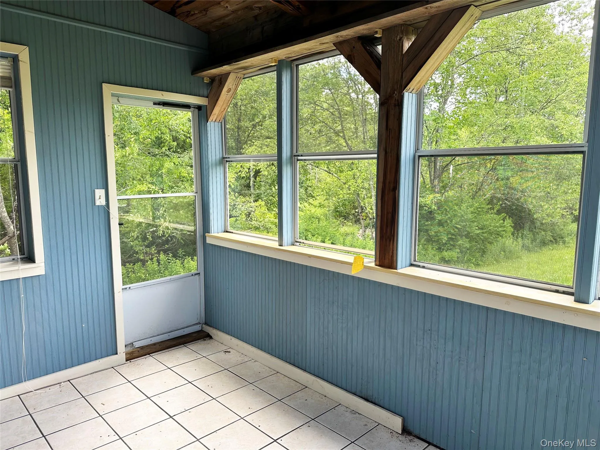 Enclosed sun room with exposed beams, panoramic woodland views, and direct outdoor access overlooking the natural landscape. Enclosed sun room with exposed beams, panoramic woodland views, and direct outdoor access overlooking the natural landscape.