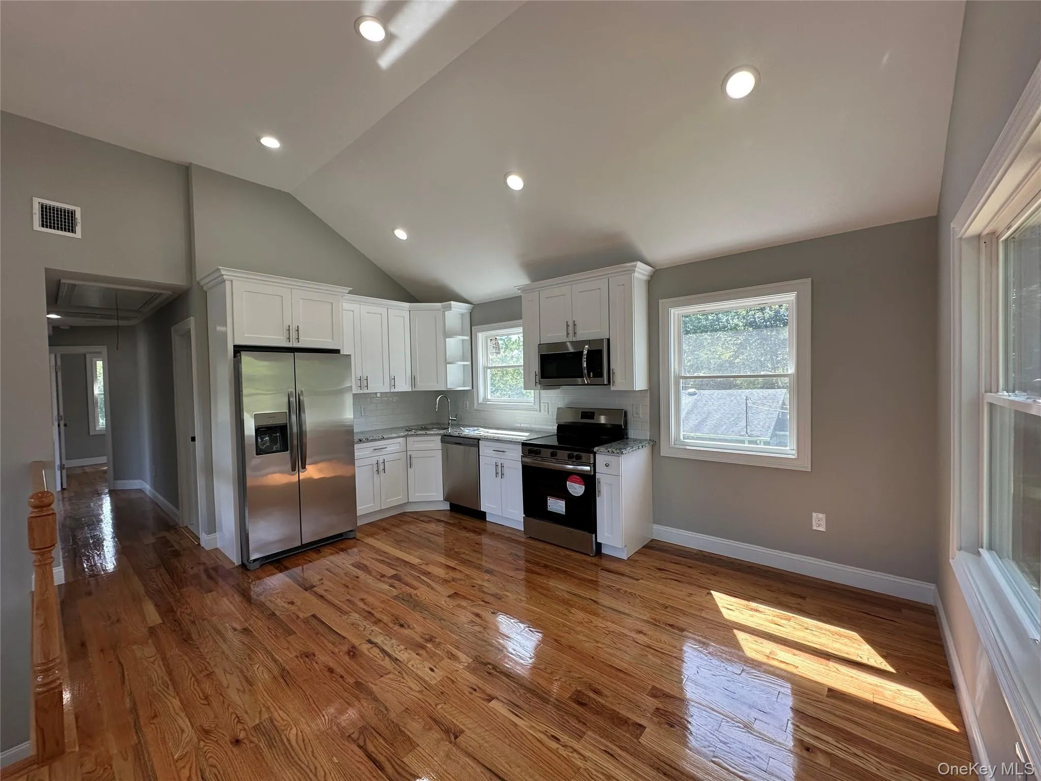Open-concept kitchen and living area featuring wood-finish flooring, white cabinetry, stainless steel appliances, and recessed lighting Open-concept kitchen and living area featuring wood-finish flooring, white cabinetry, stainless steel appliances, and recessed lighting