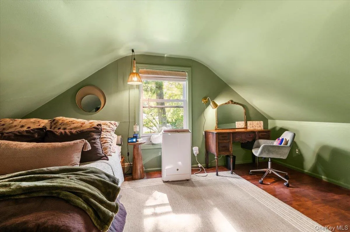 Attic space featuring sloped ceilings, hardwood flooring, and a double-pane window Attic space featuring sloped ceilings, hardwood flooring, and a double-pane window