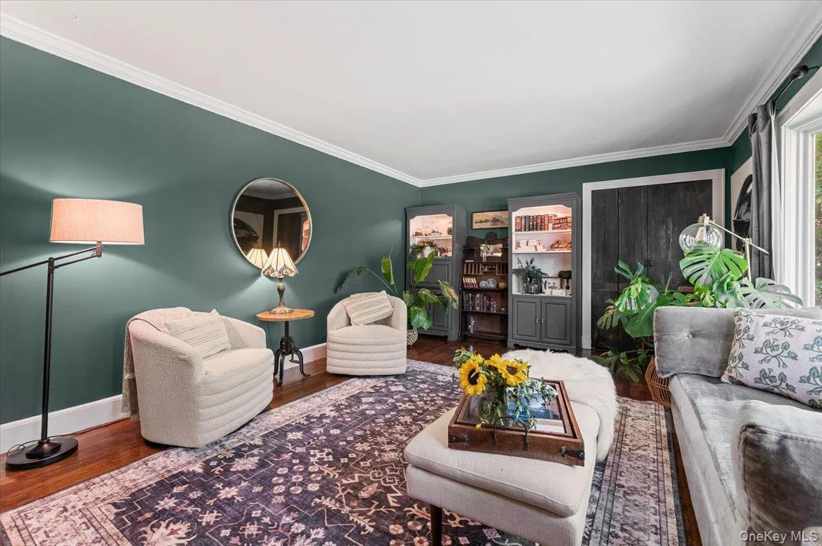 Spacious room featuring wood-finish flooring, deep green painted walls, white crown molding, and built-in shelving units with glass doors Spacious room featuring wood-finish flooring, deep green painted walls, white crown molding, and built-in shelving units with glass doors
