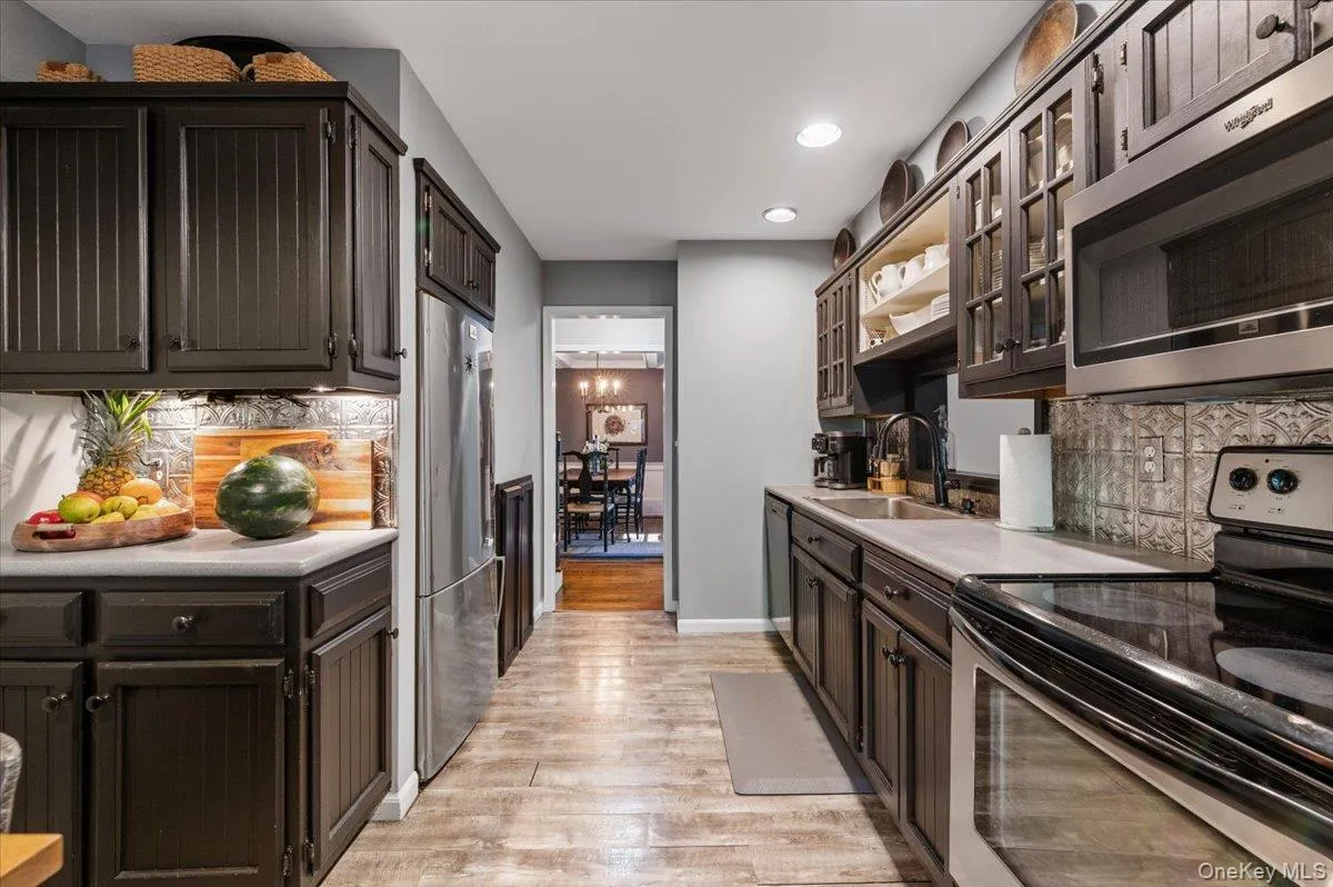Galley kitchen featuring dark wood cabinetry, stainless steel appliances, light countertops, and wood-finish flooring Galley kitchen featuring dark wood cabinetry, stainless steel appliances, light countertops, and wood-finish flooring