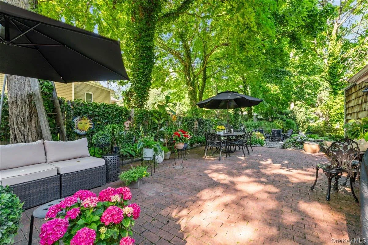 Spacious brick paver patio featuring mature trees, lush perimeter landscaping, a privacy hedge, and a shingle-sided exterior Spacious brick paver patio featuring mature trees, lush perimeter landscaping, a privacy hedge, and a shingle-sided exterior