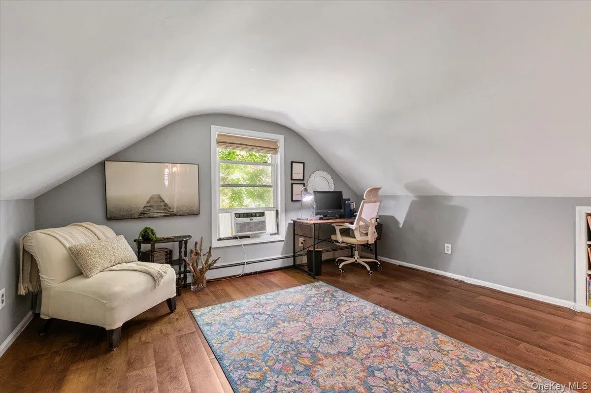 Attic living space featuring wood-finish flooring and a window with blinds Attic living space featuring wood-finish flooring and a window with blinds