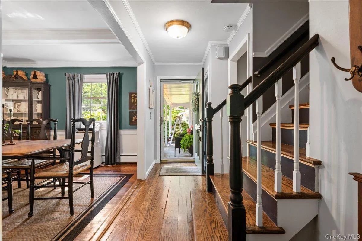 Hardwood flooring throughout entryway and dining area, featuring a staircase with contrasting dark wood handrails and white balusters, and a dining space with decorative wainscoting and a window Hardwood flooring throughout entryway and dining area, featuring a staircase with contrasting dark wood handrails and white balusters, and a dining space with decorative wainscoting and a window