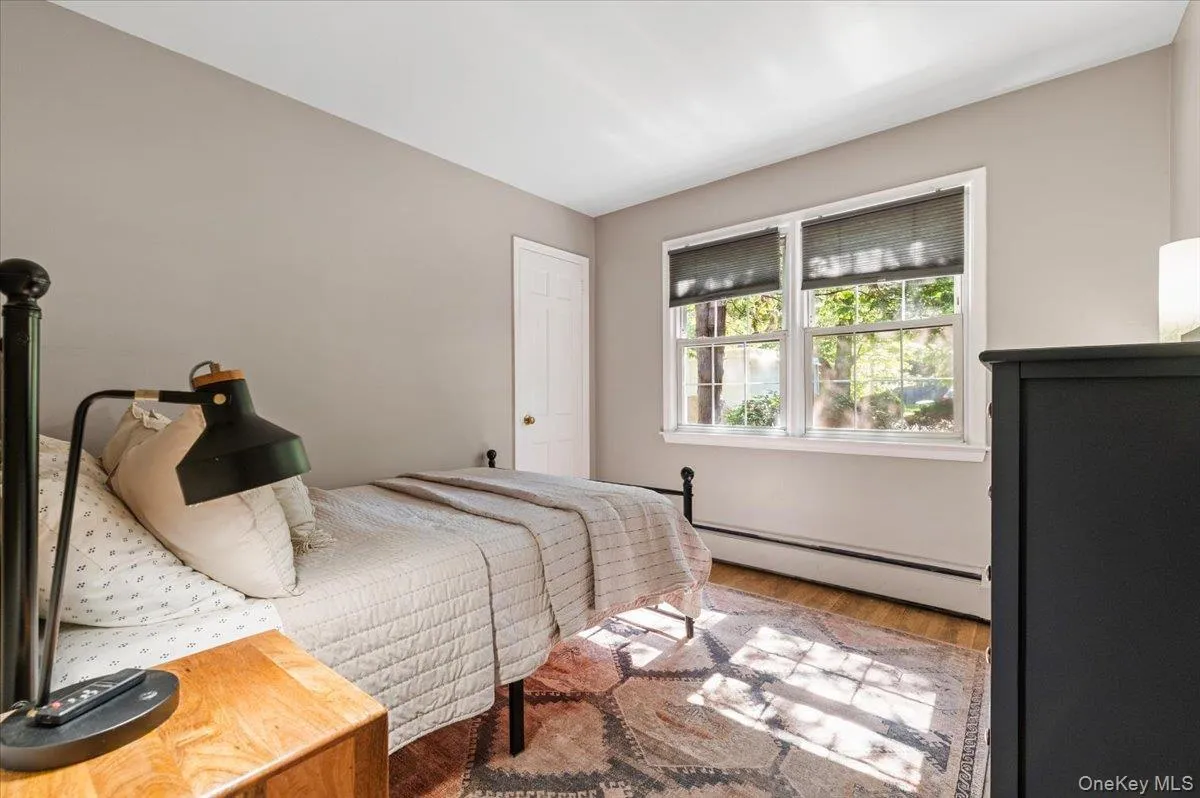 Bedroom featuring wood-finish flooring, neutral wall tones, and a double window with roller shades Bedroom featuring wood-finish flooring, neutral wall tones, and a double window with roller shades