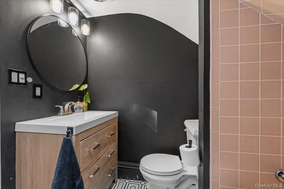 Modern bathroom featuring a wood-finish vanity with an integrated sink, brushed nickel faucet, and a circular mirror Modern bathroom featuring a wood-finish vanity with an integrated sink, brushed nickel faucet, and a circular mirror
