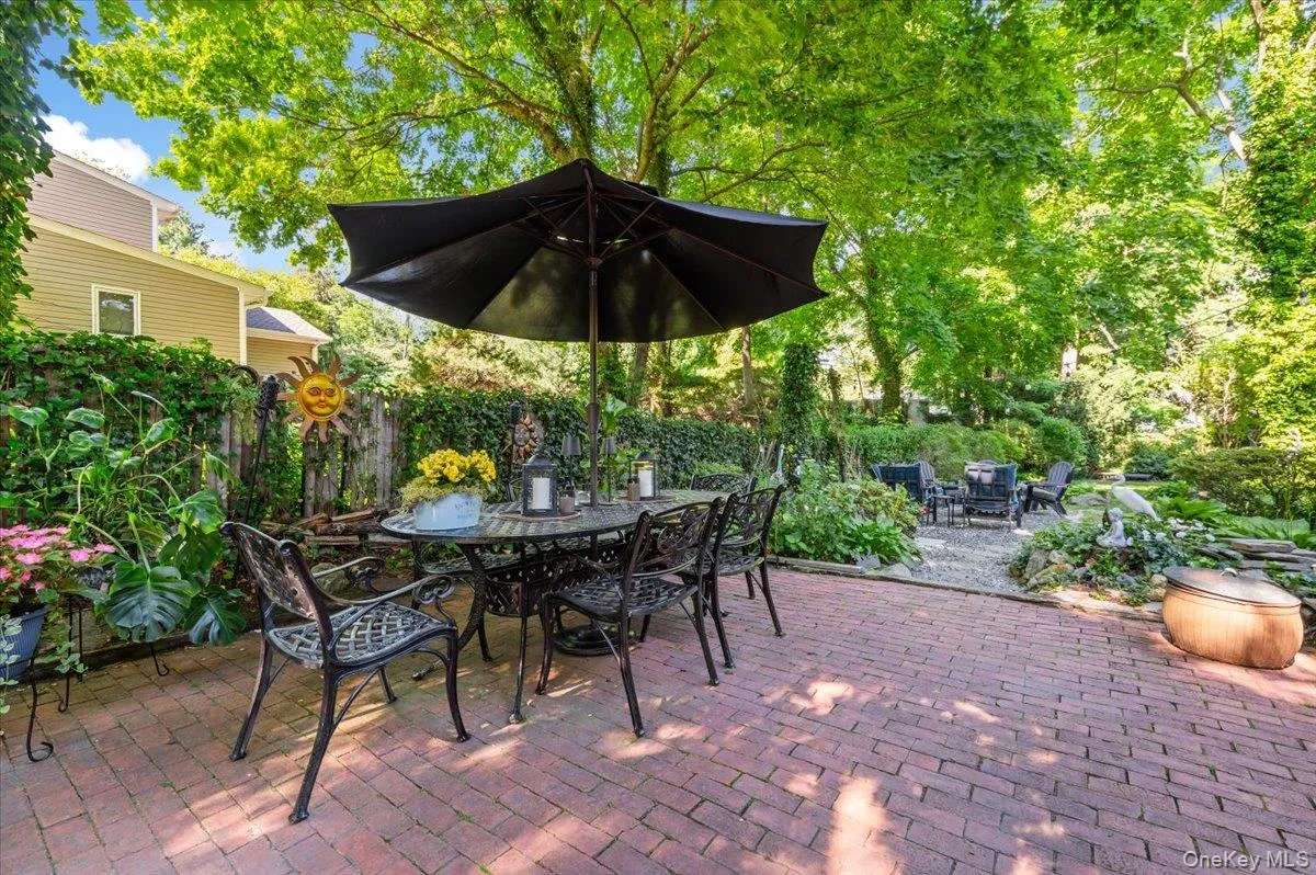 Expansive brick paver patio featuring a dining area under a large umbrella Expansive brick paver patio featuring a dining area under a large umbrella