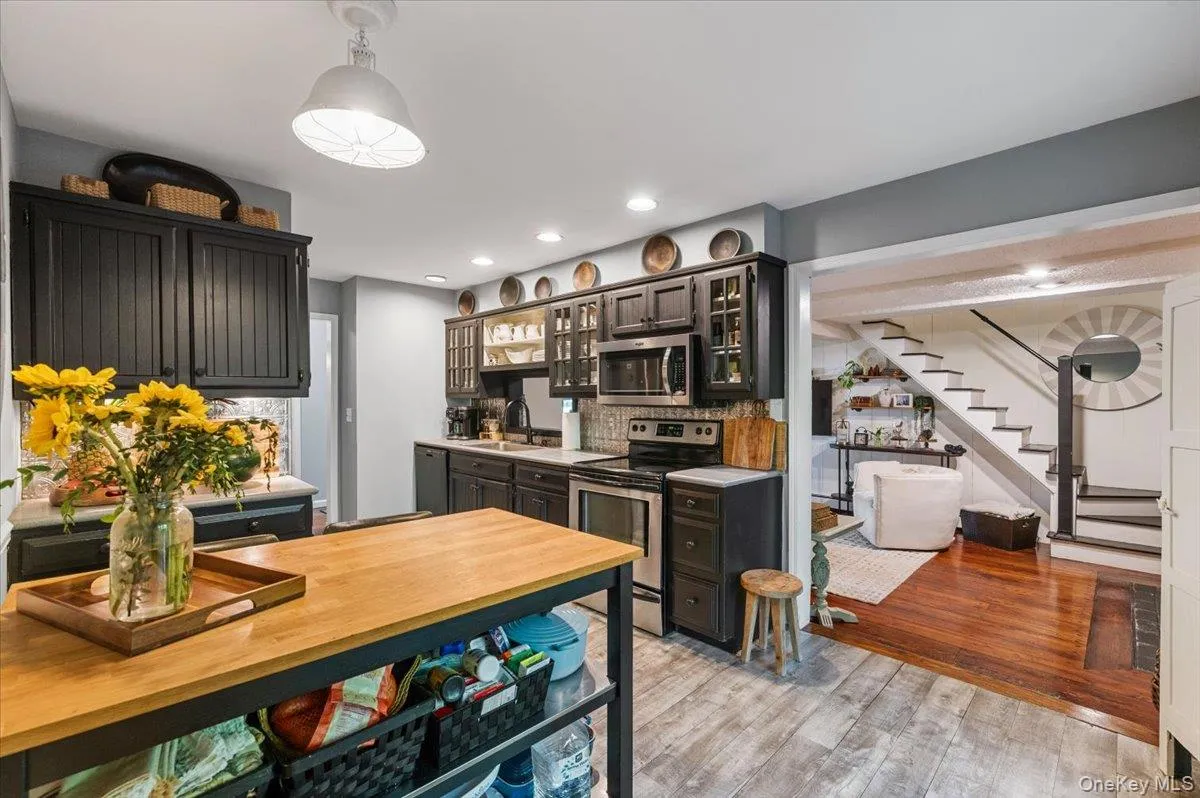Kitchen featuring dark cabinetry, stainless steel appliances, and a light wood-finish island with open shelving Kitchen featuring dark cabinetry, stainless steel appliances, and a light wood-finish island with open shelving