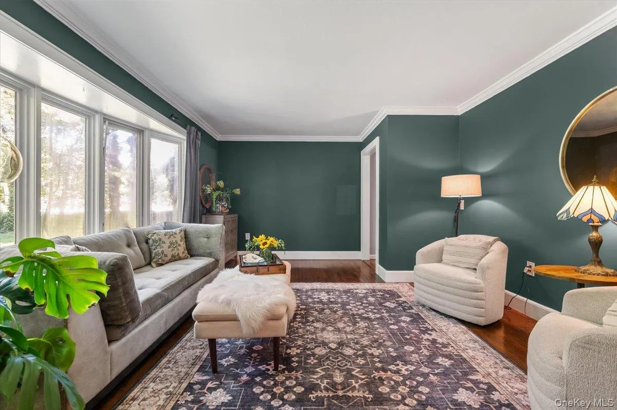 Living space featuring rich wall coloring, dark wood-finish flooring, white crown molding, and a large bay window Living space featuring rich wall coloring, dark wood-finish flooring, white crown molding, and a large bay window