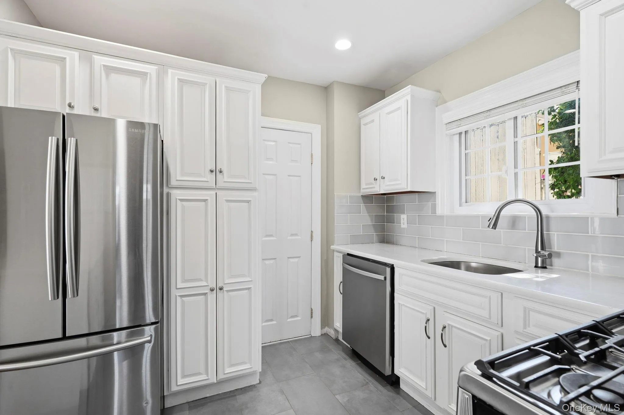 Kitchen featuring white shaker-style cabinetry, stainless steel appliances, light gray subway tile backsplash, solid surface countertops, and gray tile flooring Kitchen featuring white shaker-style cabinetry, stainless steel appliances, light gray subway tile backsplash, solid surface countertops, and gray tile flooring