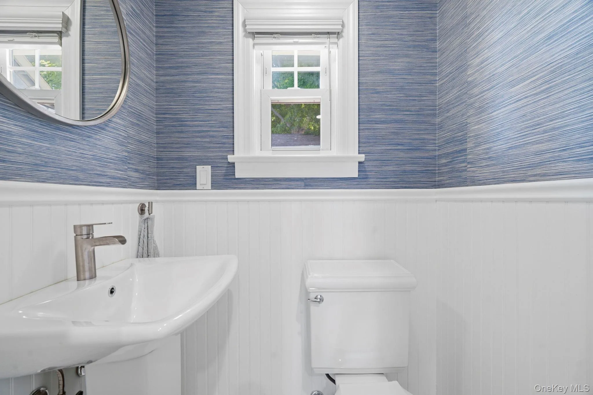 Bathroom featuring a pedestal sink with a brushed nickel faucet, a white toilet, and a window with white trim Bathroom featuring a pedestal sink with a brushed nickel faucet, a white toilet, and a window with white trim