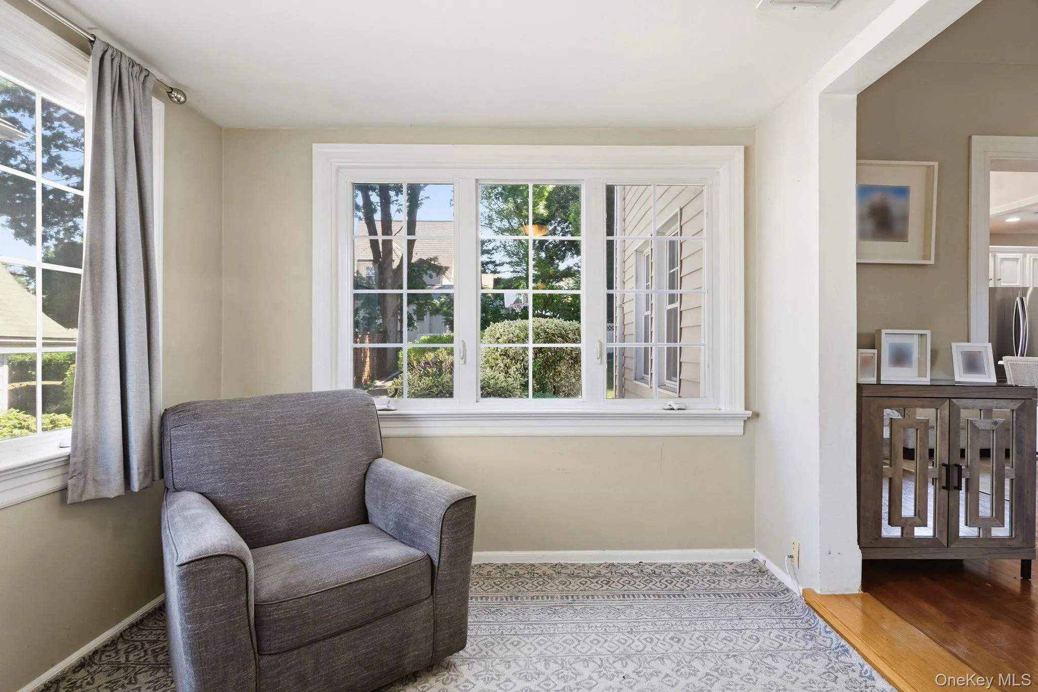 Interior room featuring two multi-pane windows with white trim, light beige wall paint, and a patterned area rug Interior room featuring two multi-pane windows with white trim, light beige wall paint, and a patterned area rug