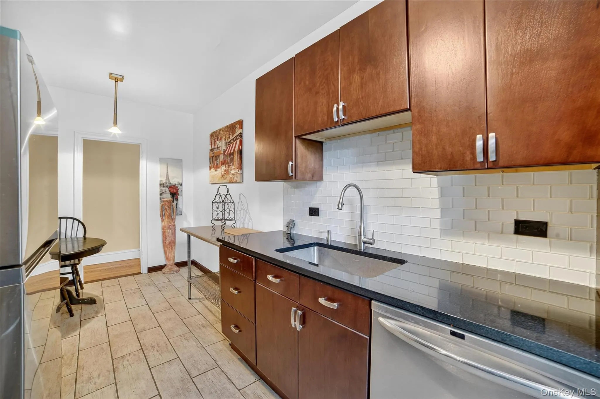 Kitchen featuring decorative backsplash, stainless steel appliances, pendant lighting, dark stone countertops, and light wood-style floors Kitchen featuring decorative backsplash, stainless steel appliances, pendant lighting, dark stone countertops, and light wood-style floors