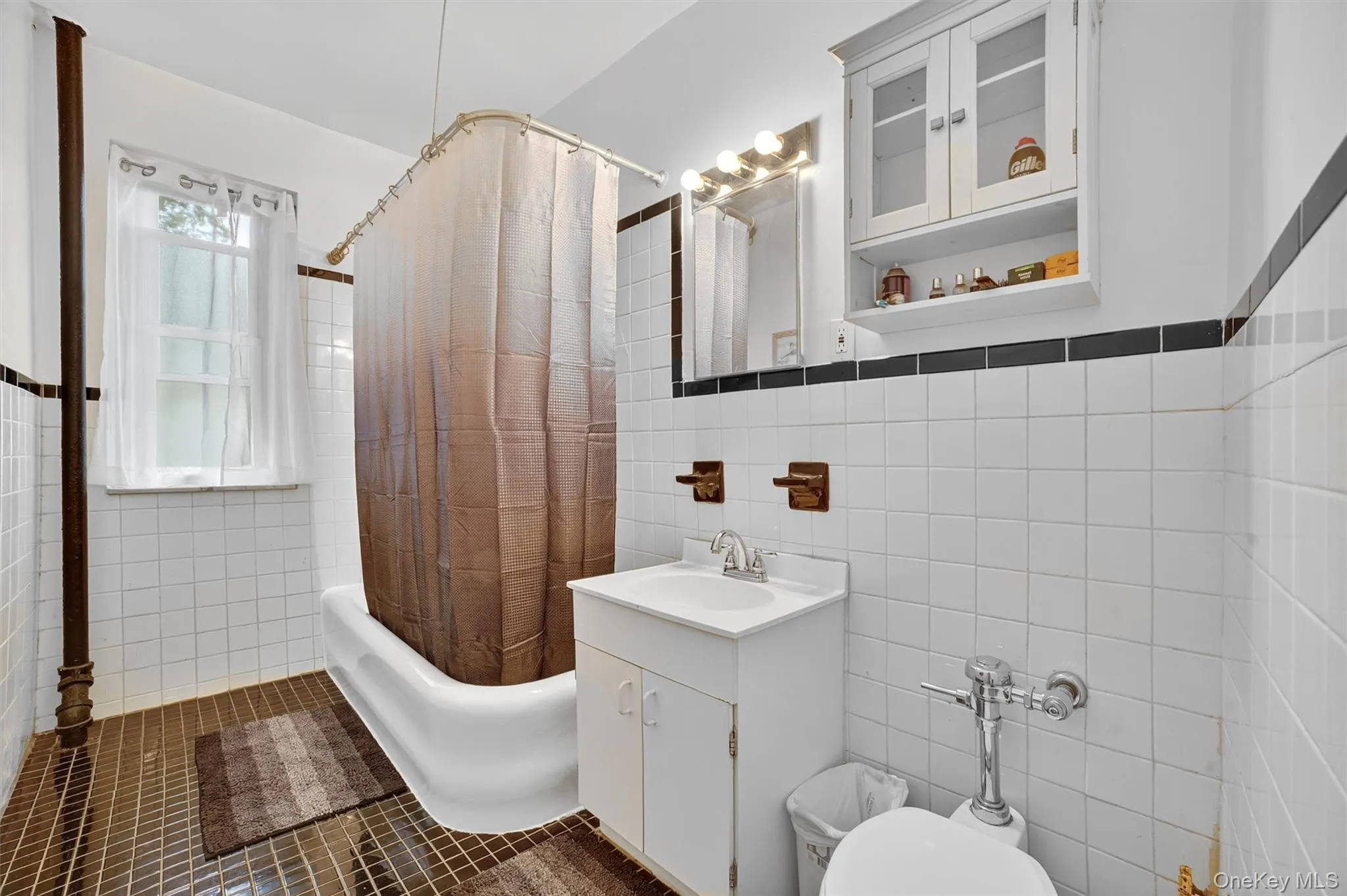 Full bathroom with tile walls, shower / bathtub combination with curtain, vanity, and dark tile patterned flooring Full bathroom with tile walls, shower / bathtub combination with curtain, vanity, and dark tile patterned flooring