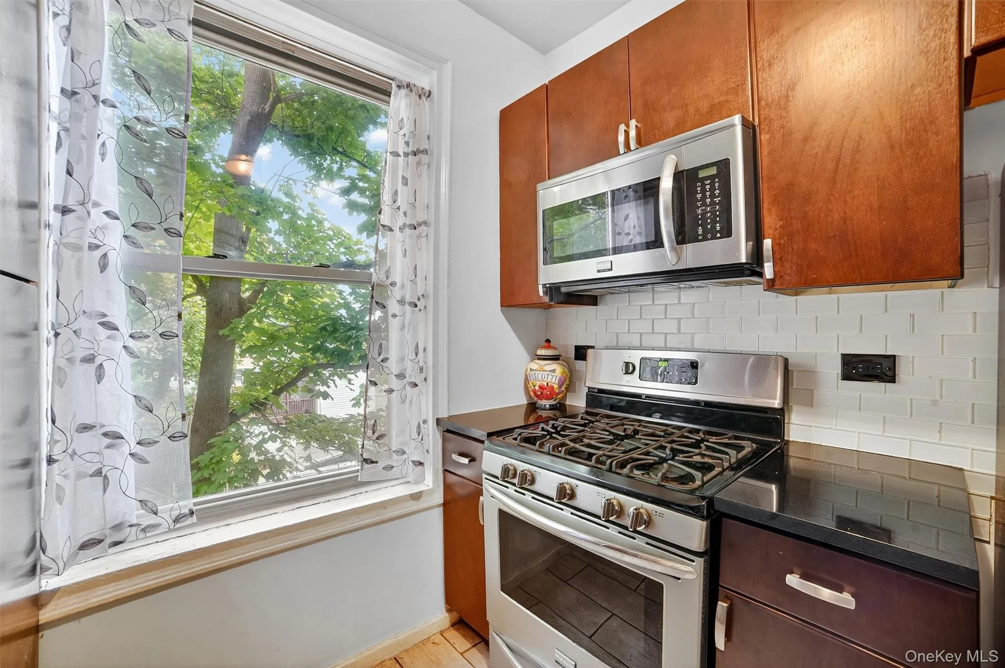 Kitchen featuring healthy amount of natural light, stainless steel appliances, tasteful backsplash, and brown cabinetry Kitchen featuring healthy amount of natural light, stainless steel appliances, tasteful backsplash, and brown cabinetry