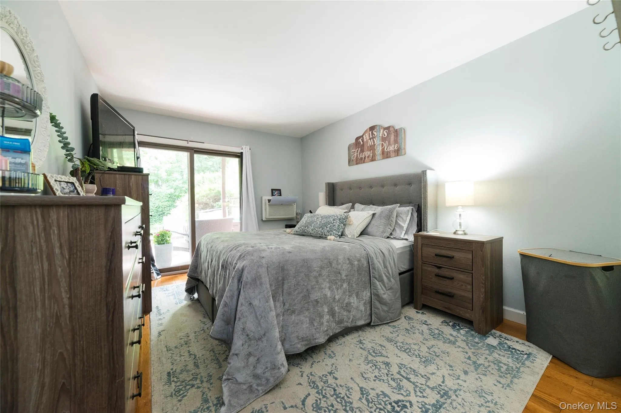 Primary bedroom featuring wood-finish flooring, a sliding glass door leading to private outdoor space, and a through wall-sleeve air conditioning unit Primary bedroom featuring wood-finish flooring, a sliding glass door leading to private outdoor space, and a through wall-sleeve air conditioning unit