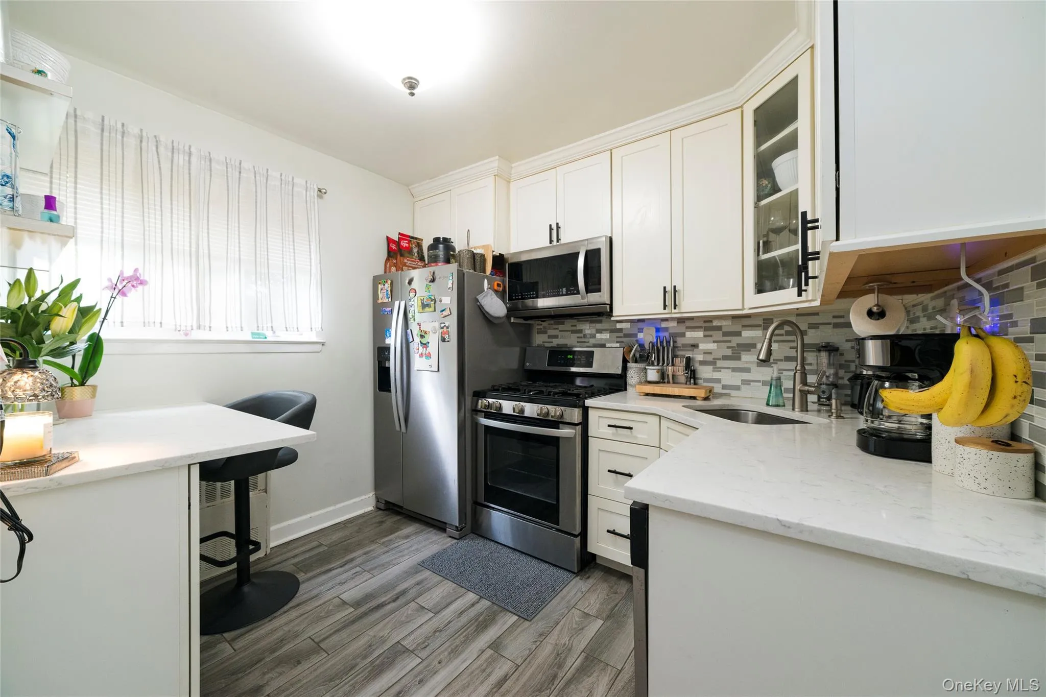 Modern kitchen featuring vinyl-finish flooring, white cabinetry with black hardware, stainless steel appliances, and quartz countertops Modern kitchen featuring vinyl-finish flooring, white cabinetry with black hardware, stainless steel appliances, and quartz countertops