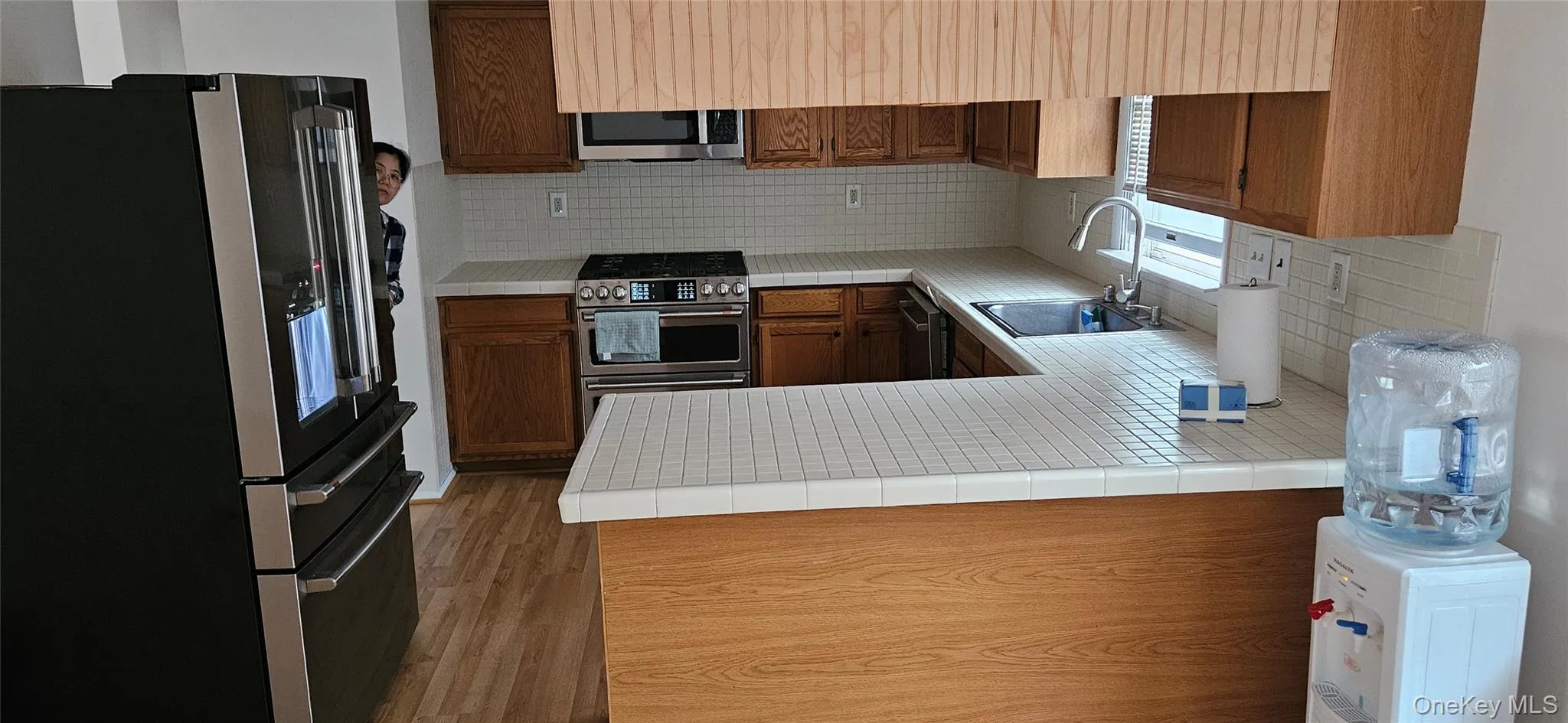 Kitchen featuring wood cabinetry, stainless steel appliances, tile countertops, and a white tile backsplash Kitchen featuring wood cabinetry, stainless steel appliances, tile countertops, and a white tile backsplash