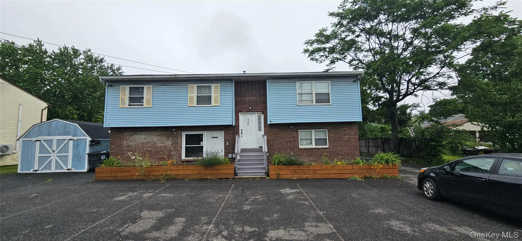 Two-story property featuring light blue siding with white trim, brick facade, a central white entry door, and a dedicated parking area Two-story property featuring light blue siding with white trim, brick facade, a central white entry door, and a dedicated parking area