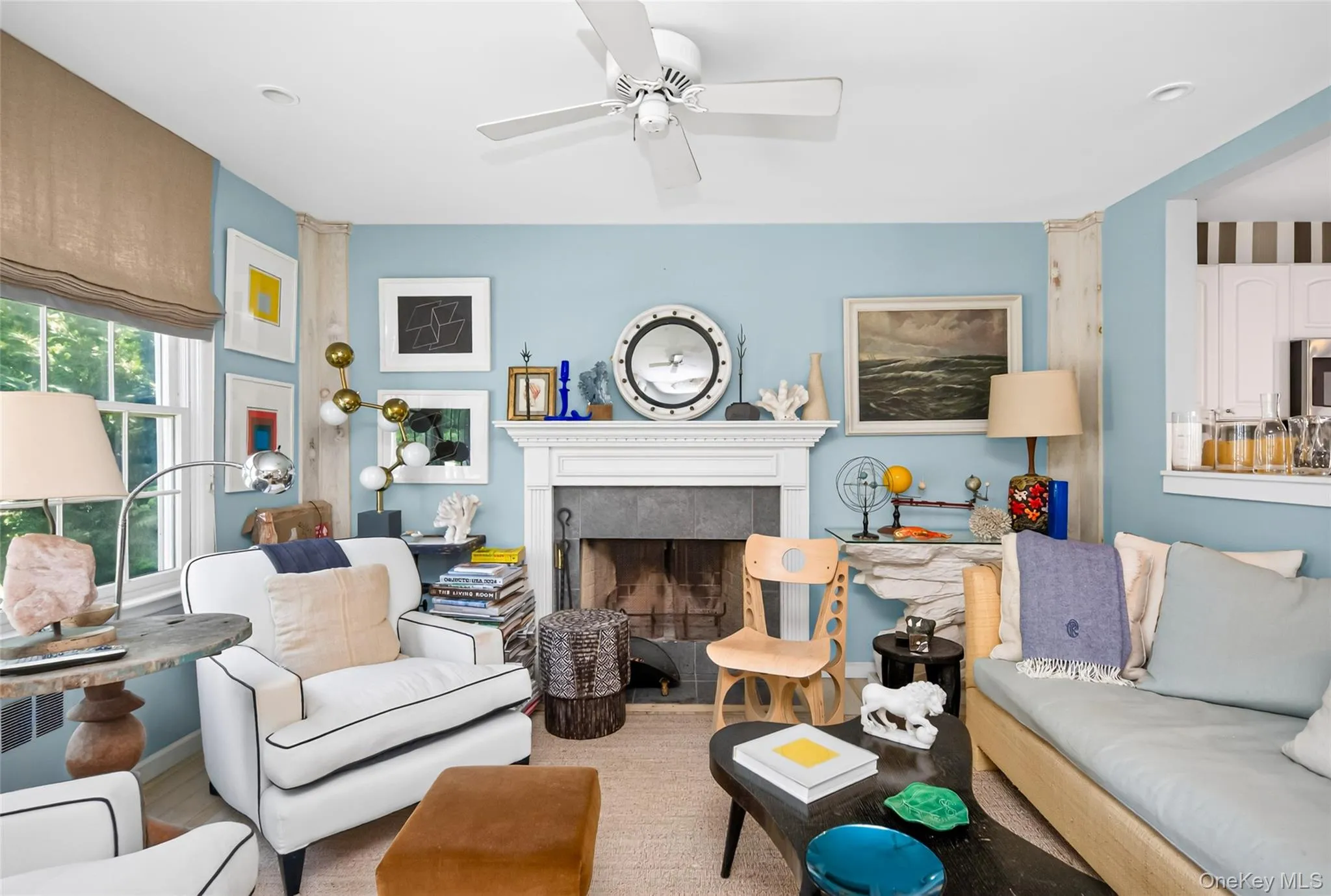 Living area featuring a white ceiling fan, light blue walls, and a fireplace with a white mantel and stone surround Living area featuring a white ceiling fan, light blue walls, and a fireplace with a white mantel and stone surround