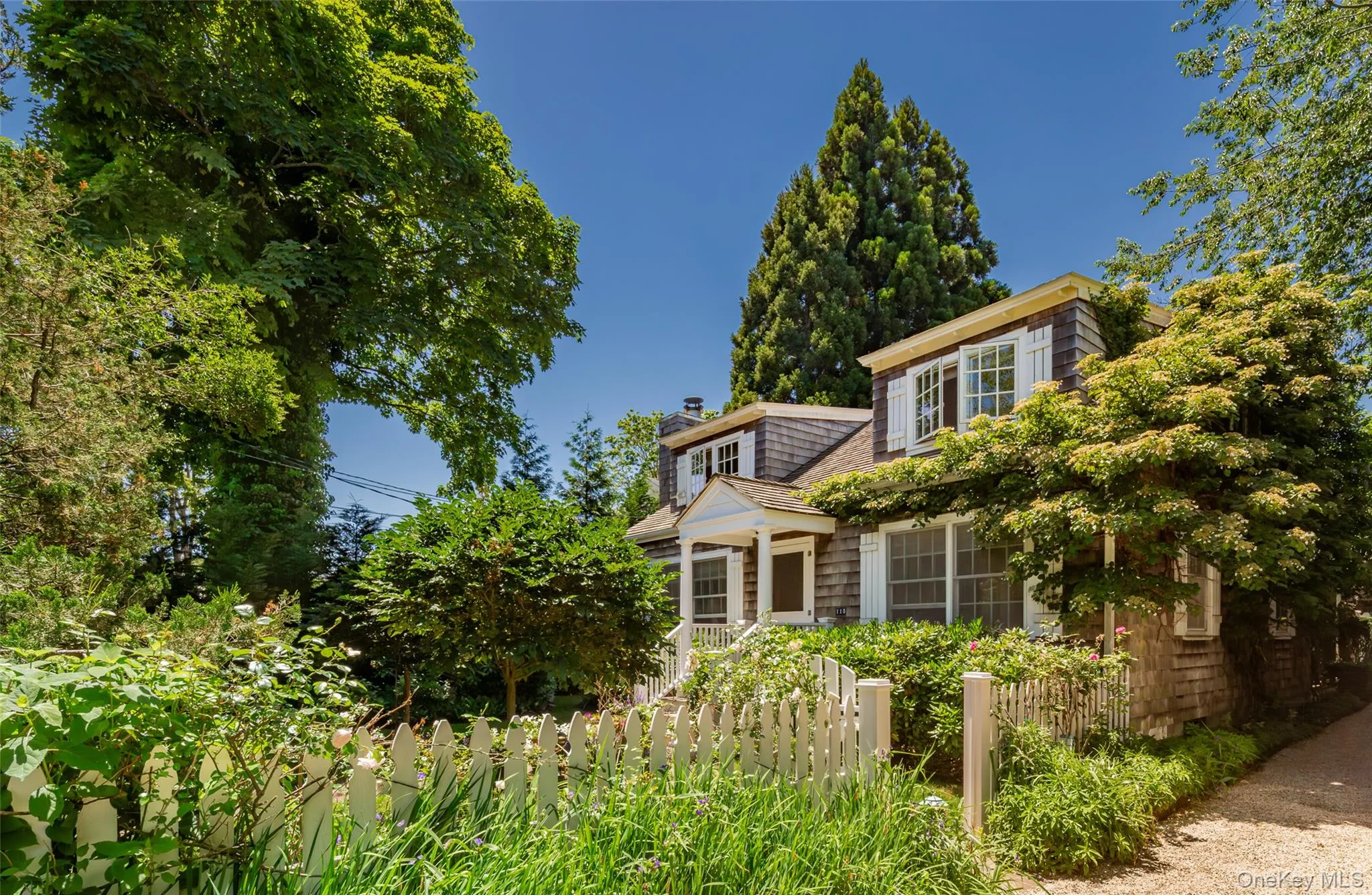 Shingle-sided residence with white picket fence and mature landscaping Shingle-sided residence with white picket fence and mature landscaping