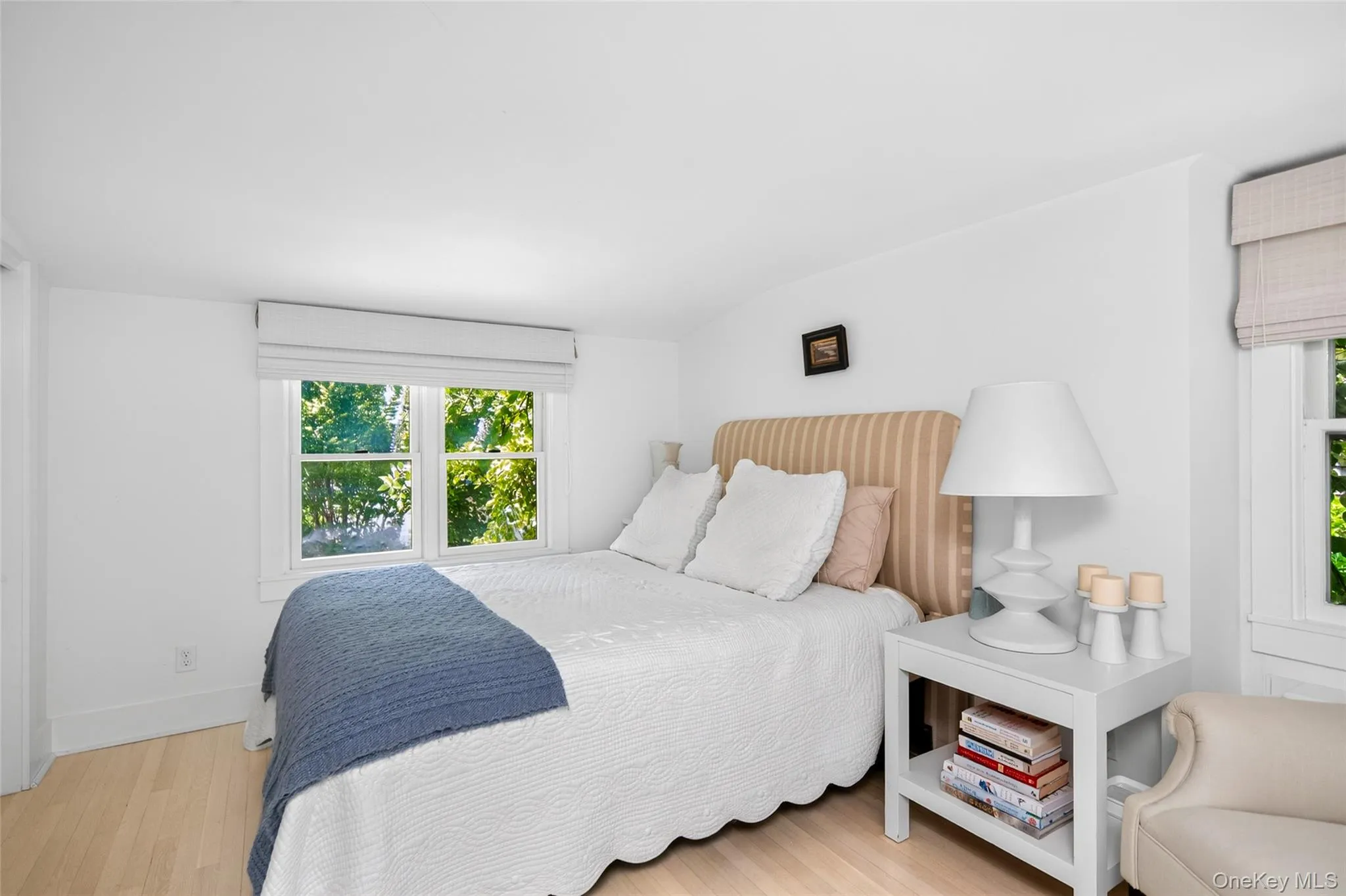 Bright 2nd floor bedroom with wood-finish flooring, white walls, and two windows featuring light-colored Roman shades Bright 2nd floor bedroom with wood-finish flooring, white walls, and two windows featuring light-colored Roman shades