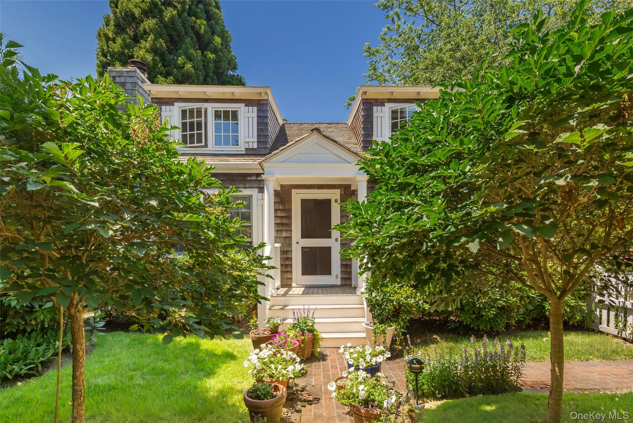 Shingle-style cottage featuring a gabled entry, white trim, and multi-pane windows with decorative shutters Shingle-style cottage featuring a gabled entry, white trim, and multi-pane windows with decorative shutters