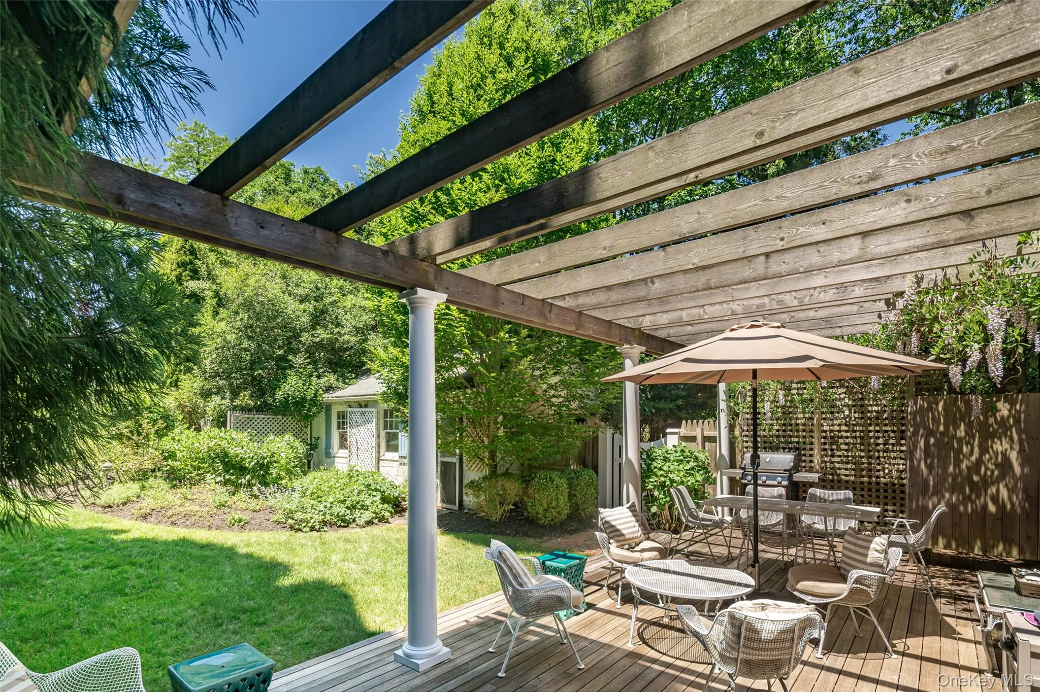Expansive backyard featuring a wood deck with a pergola, a manicured lawn, and mature trees Expansive backyard featuring a wood deck with a pergola, a manicured lawn, and mature trees
