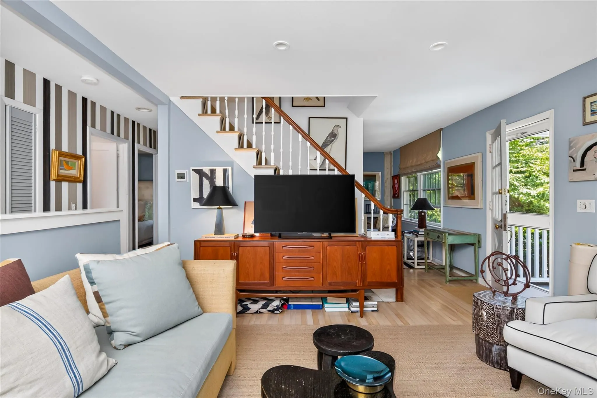 Open-concept living space with light wood-finish flooring, a contemporary staircase featuring white risers and wood treads, and white balusters Open-concept living space with light wood-finish flooring, a contemporary staircase featuring white risers and wood treads, and white balusters