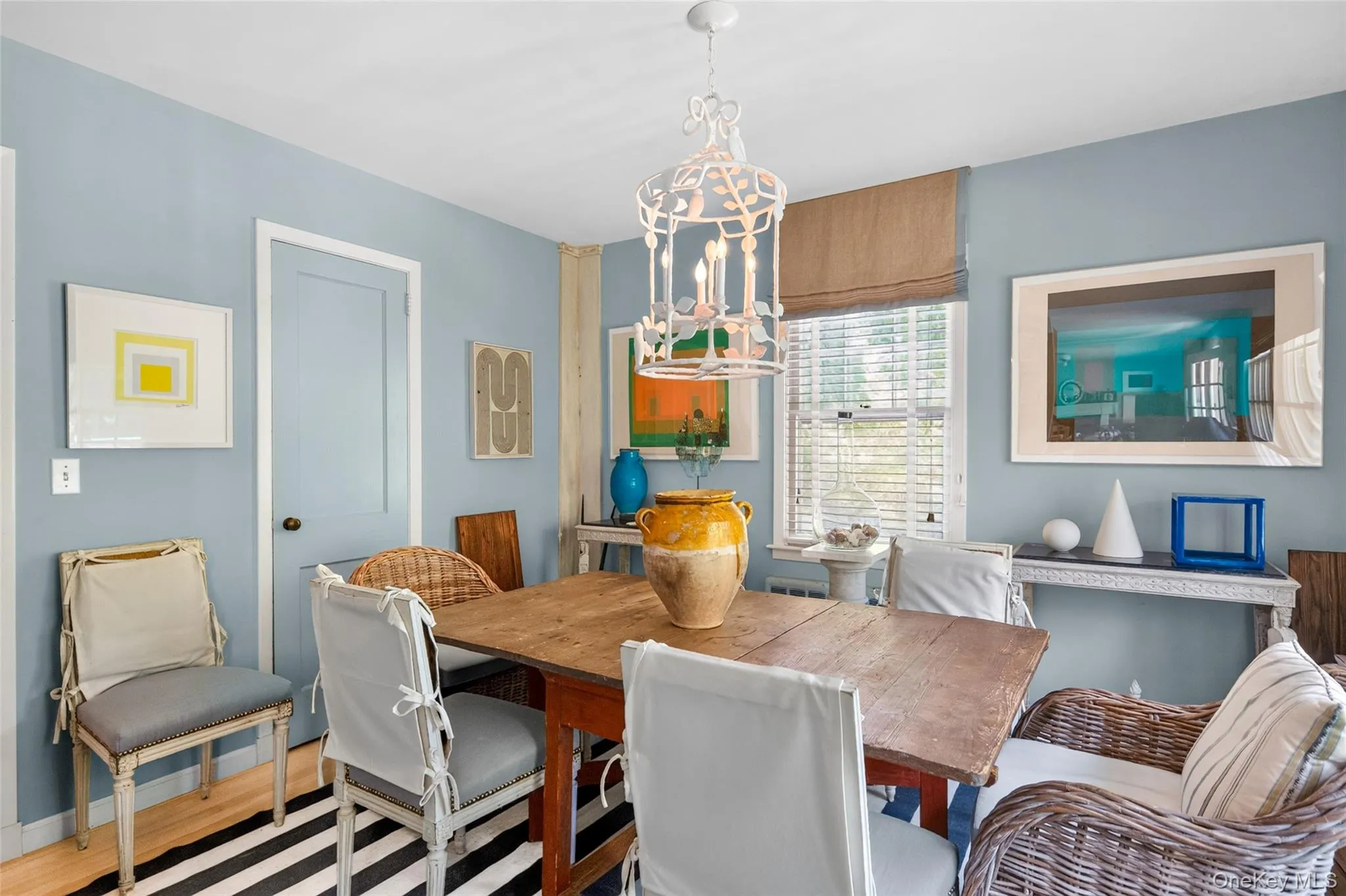 Dining area featuring light blue walls, a white decorative chandelier, a wood-finish table, and a window with blinds Dining area featuring light blue walls, a white decorative chandelier, a wood-finish table, and a window with blinds