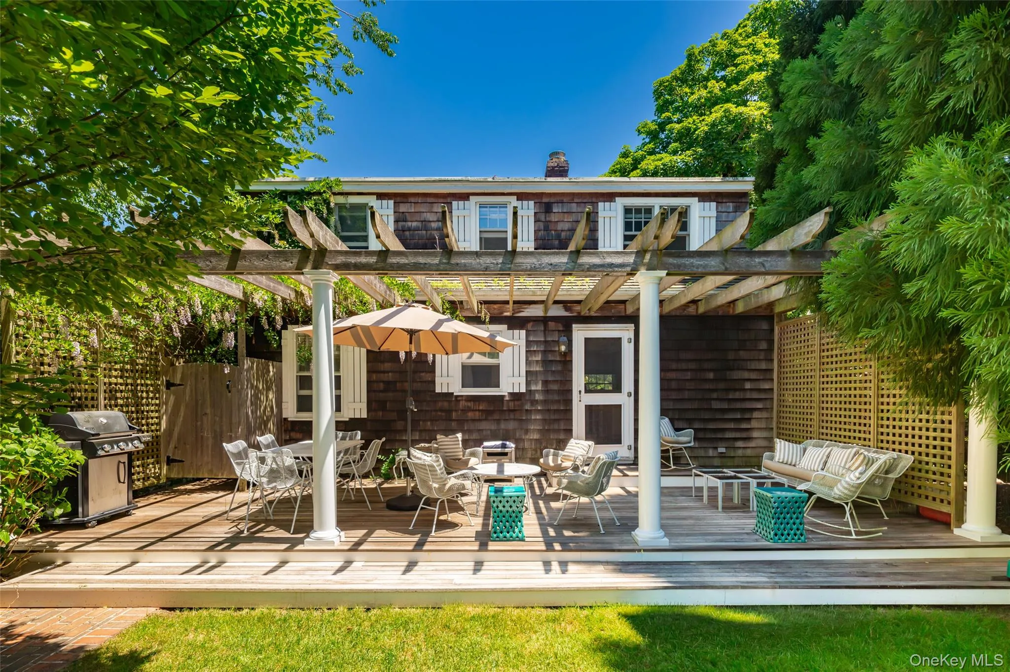 Expansive wood-finish deck with pergola structure, white columns, and a lattice privacy screen Expansive wood-finish deck with pergola structure, white columns, and a lattice privacy screen