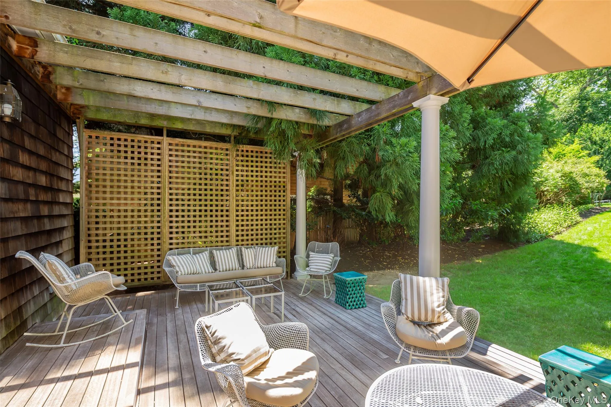 Spacious outdoor deck featuring natural wood flooring, a slatted pergola, a decorative privacy screen, a column support, and an attached umbrella for shade Spacious outdoor deck featuring natural wood flooring, a slatted pergola, a decorative privacy screen, a column support, and an attached umbrella for shade