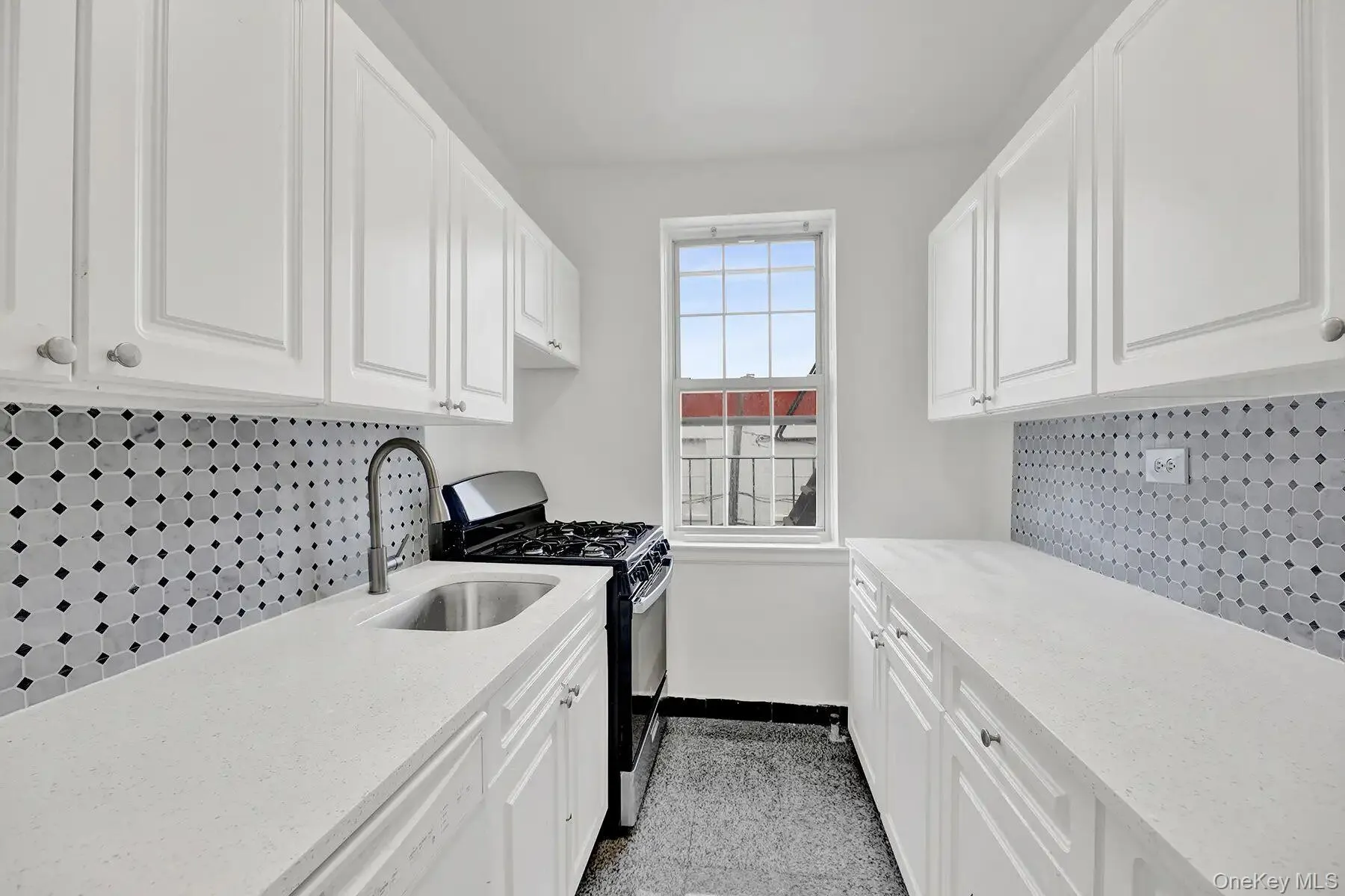 Galley kitchen featuring white cabinetry with brushed nickel hardware, light-toned countertops, and a patterned tile backsplash Galley kitchen featuring white cabinetry with brushed nickel hardware, light-toned countertops, and a patterned tile backsplash
