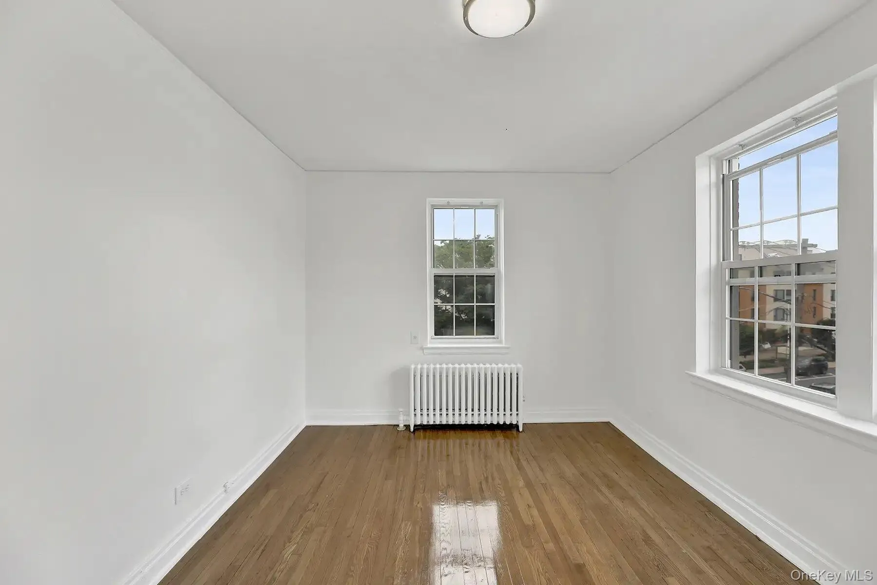 Bright room featuring two windows, wood-finish flooring, and white baseboards Bright room featuring two windows, wood-finish flooring, and white baseboards