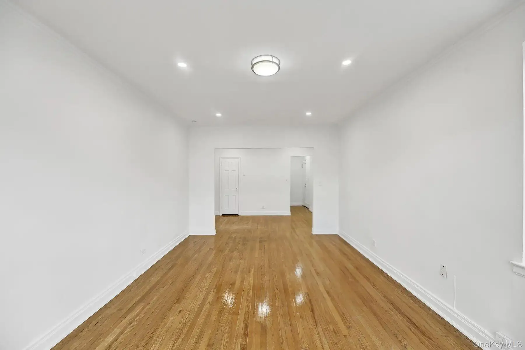 Spacious room featuring wood-finish flooring, white baseboards, crown molding, recessed lighting, and a flush mount ceiling fixture Spacious room featuring wood-finish flooring, white baseboards, crown molding, recessed lighting, and a flush mount ceiling fixture