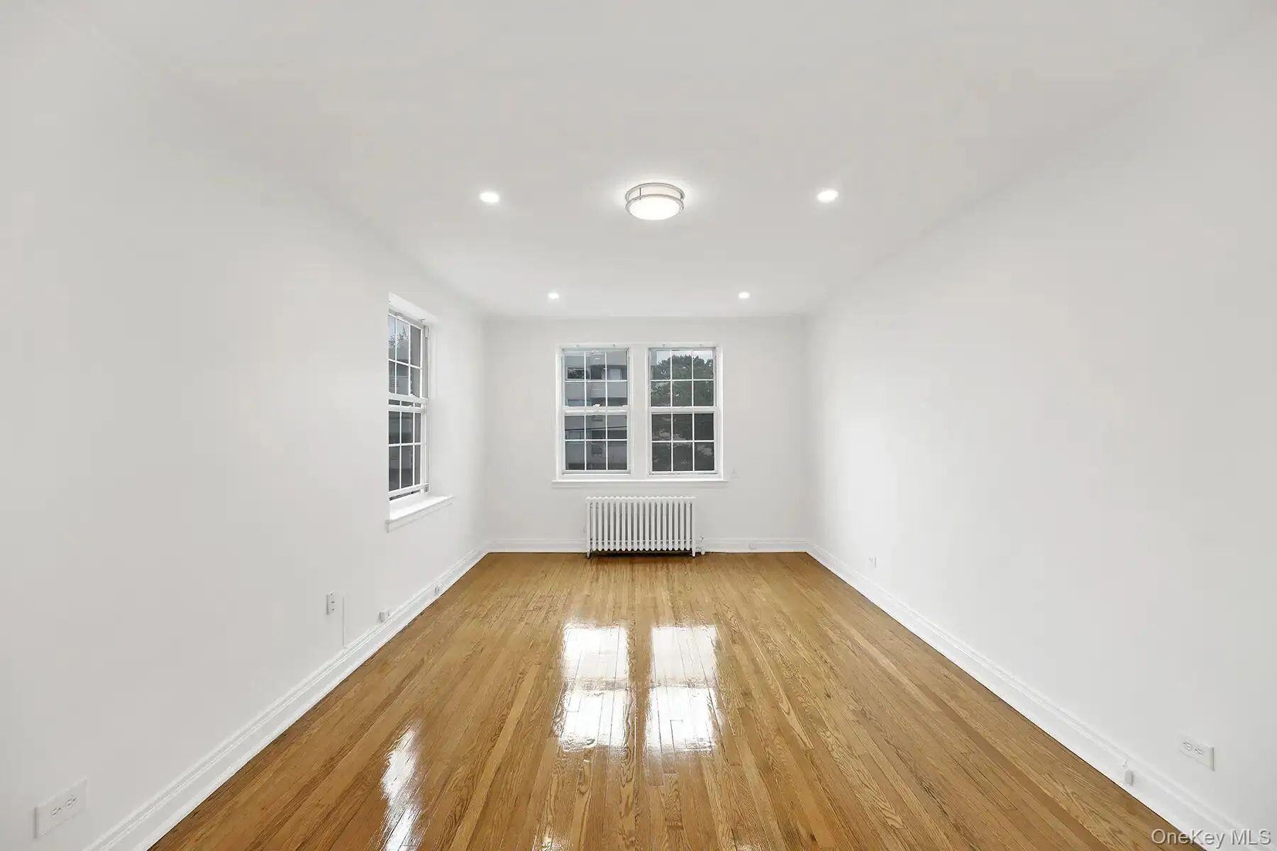 Bright room featuring wood-finish flooring, white walls, and multiple windows Bright room featuring wood-finish flooring, white walls, and multiple windows