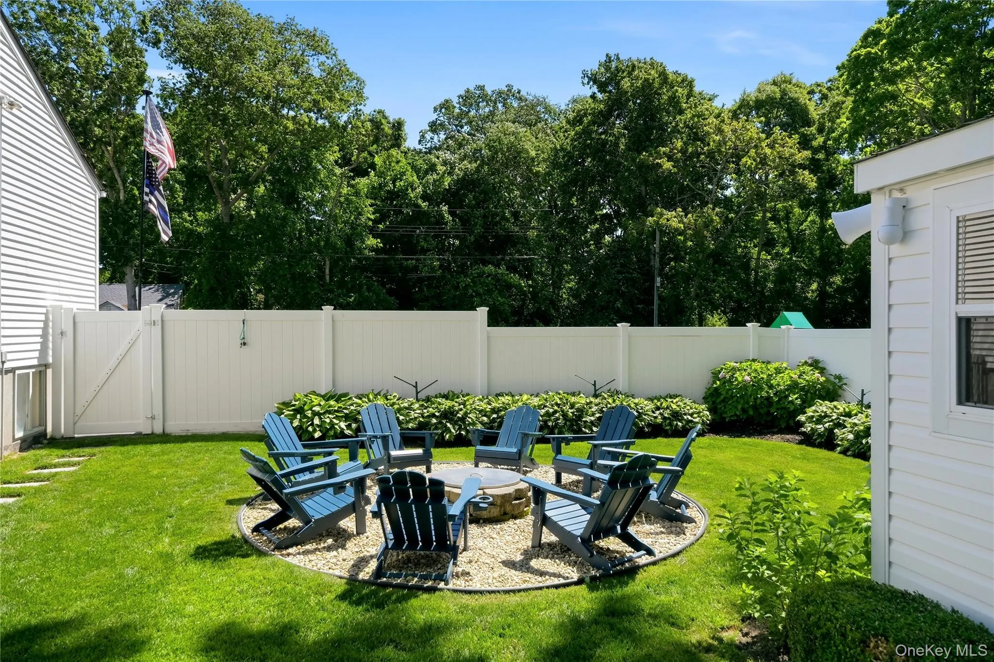 Expansive backyard featuring a central fire pit area with gravel hardscaping, surrounded by lush green lawn Expansive backyard featuring a central fire pit area with gravel hardscaping, surrounded by lush green lawn