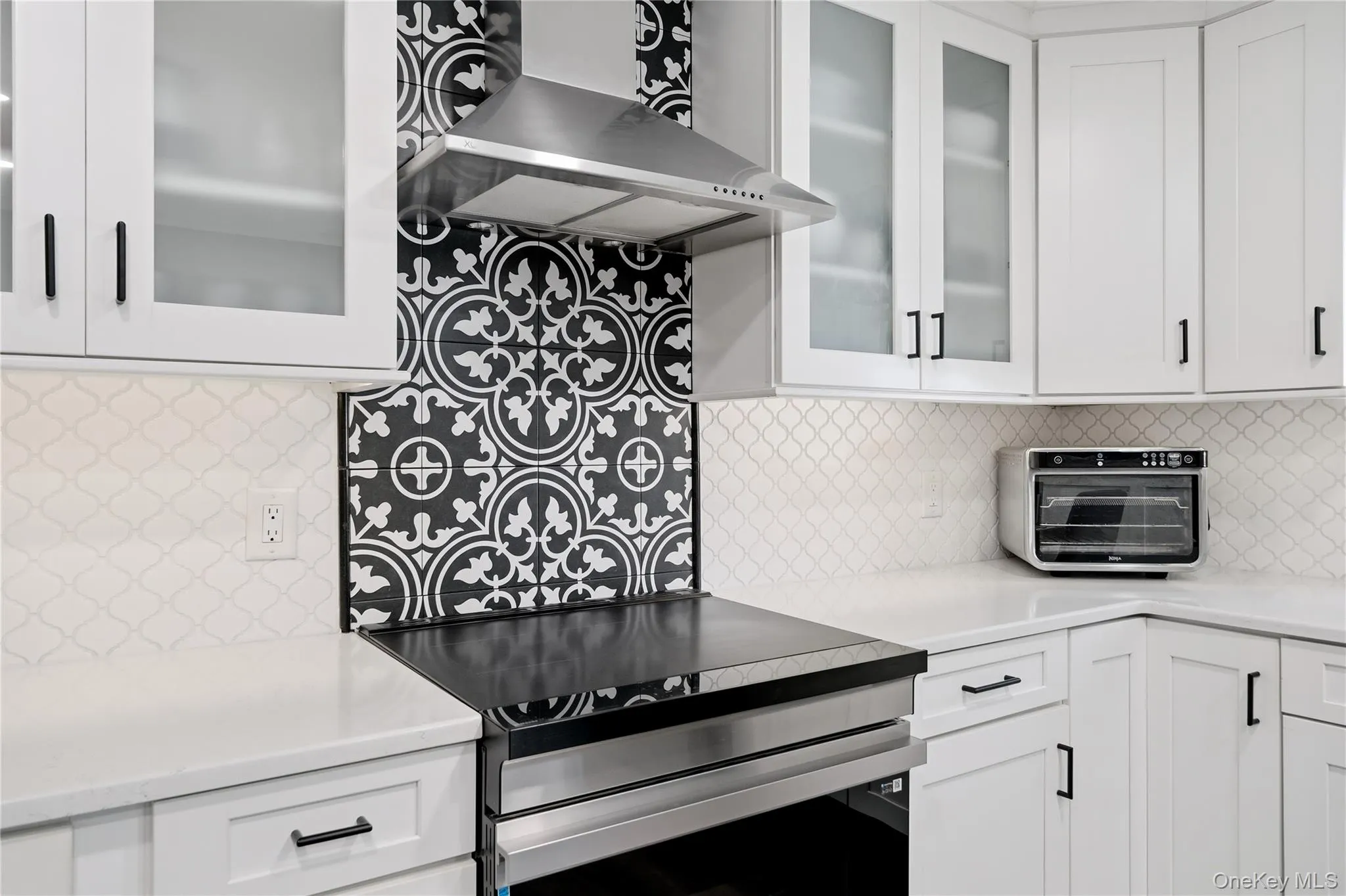 Kitchen featuring white cabinetry with black hardware, white countertops, and a black and white patterned tile backsplash Kitchen featuring white cabinetry with black hardware, white countertops, and a black and white patterned tile backsplash
