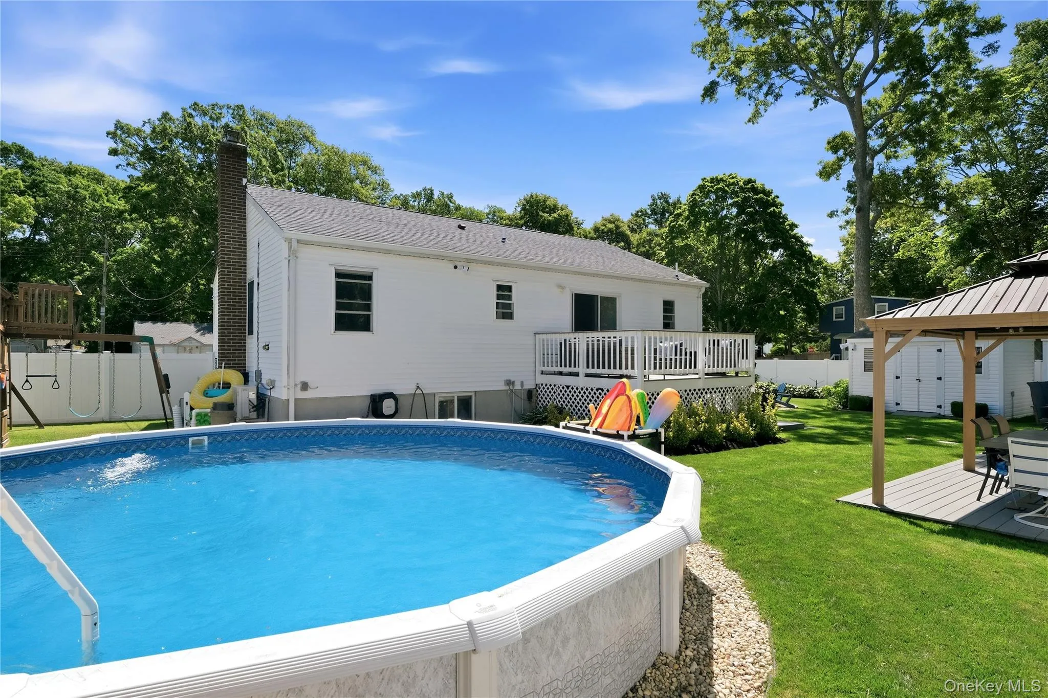 Expansive backyard featuring an above-ground swimming pool, a wooden deck, a gazebo, and verdant lawn Expansive backyard featuring an above-ground swimming pool, a wooden deck, a gazebo, and verdant lawn