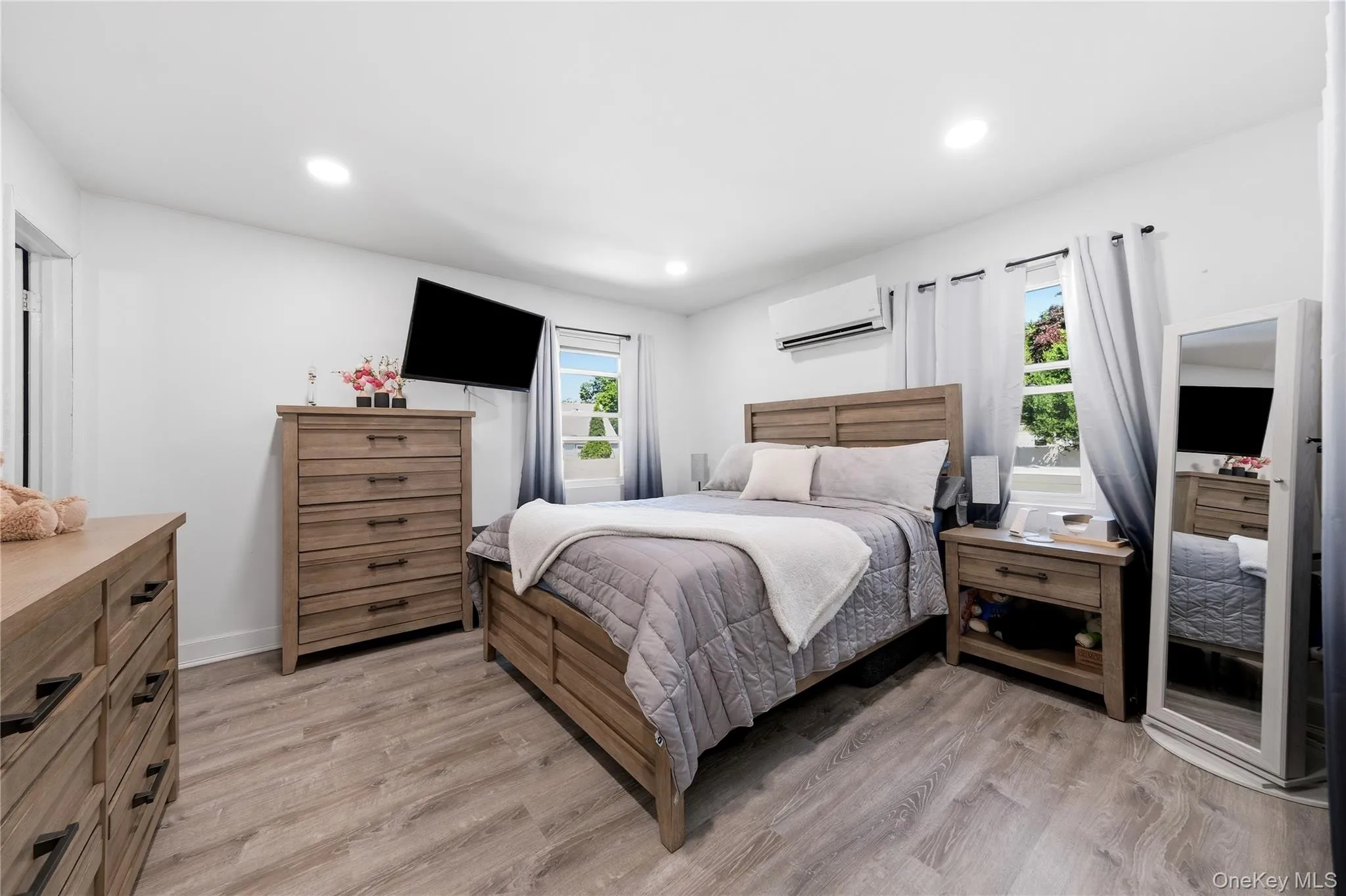 Spacious bedroom featuring wood-finish flooring, recessed lighting, and bright white walls Spacious bedroom featuring wood-finish flooring, recessed lighting, and bright white walls