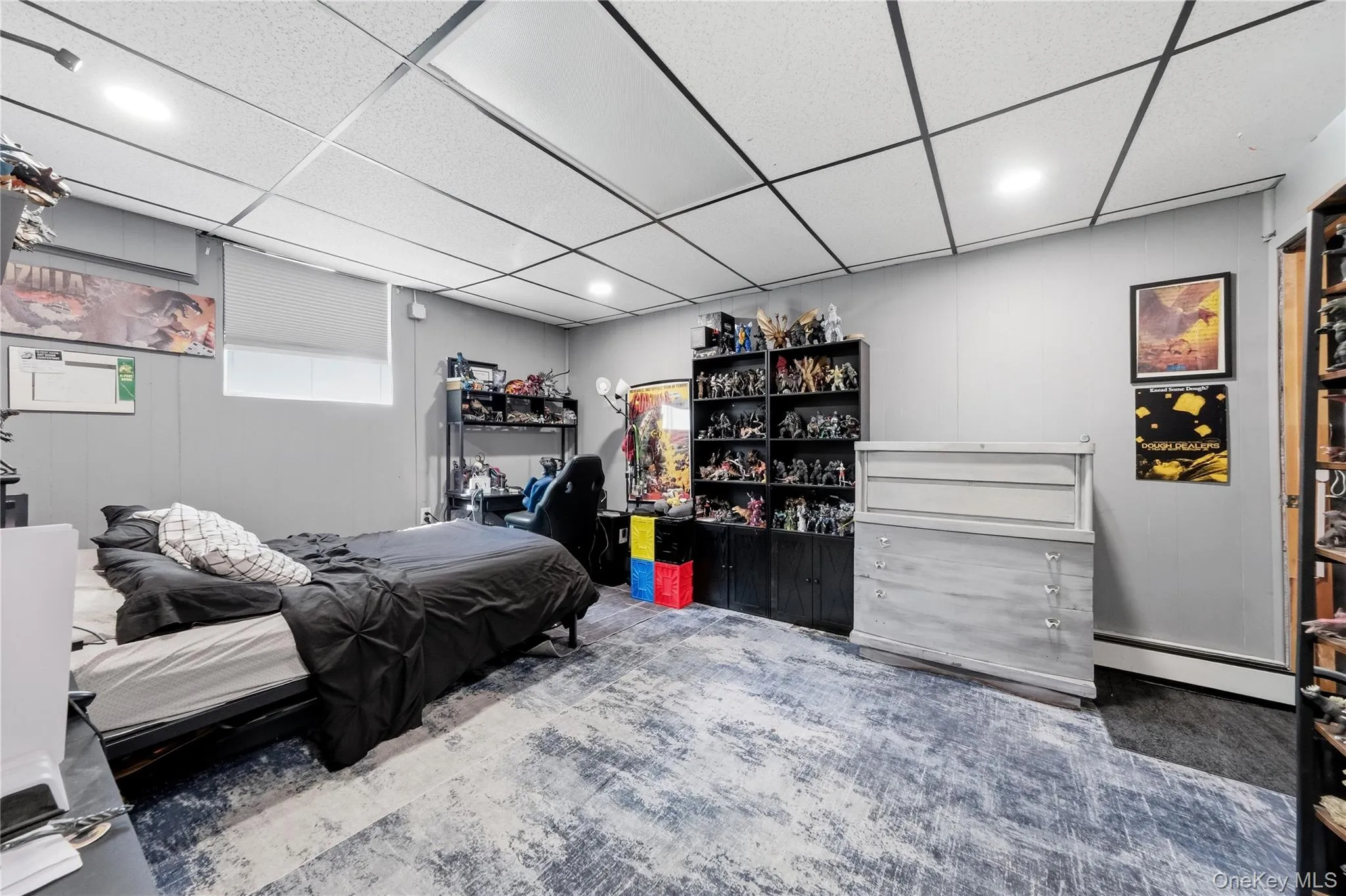 Spacious room featuring a drop ceiling with recessed lighting, gray wall paneling, and a large window with a roller shade Spacious room featuring a drop ceiling with recessed lighting, gray wall paneling, and a large window with a roller shade