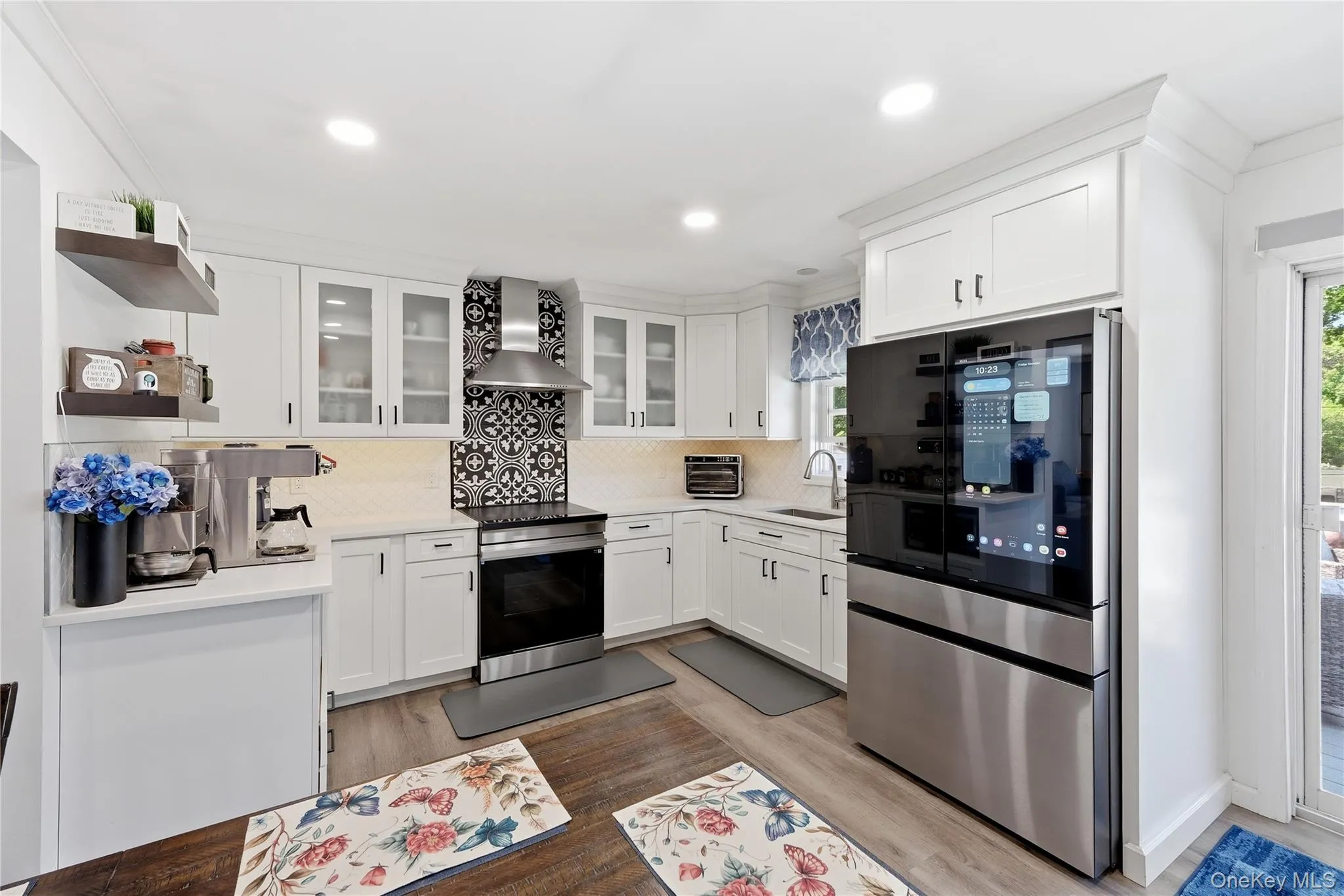 Modern kitchen featuring white shaker cabinetry, stainless steel appliances, light-toned countertops, and wood-finish flooring Modern kitchen featuring white shaker cabinetry, stainless steel appliances, light-toned countertops, and wood-finish flooring