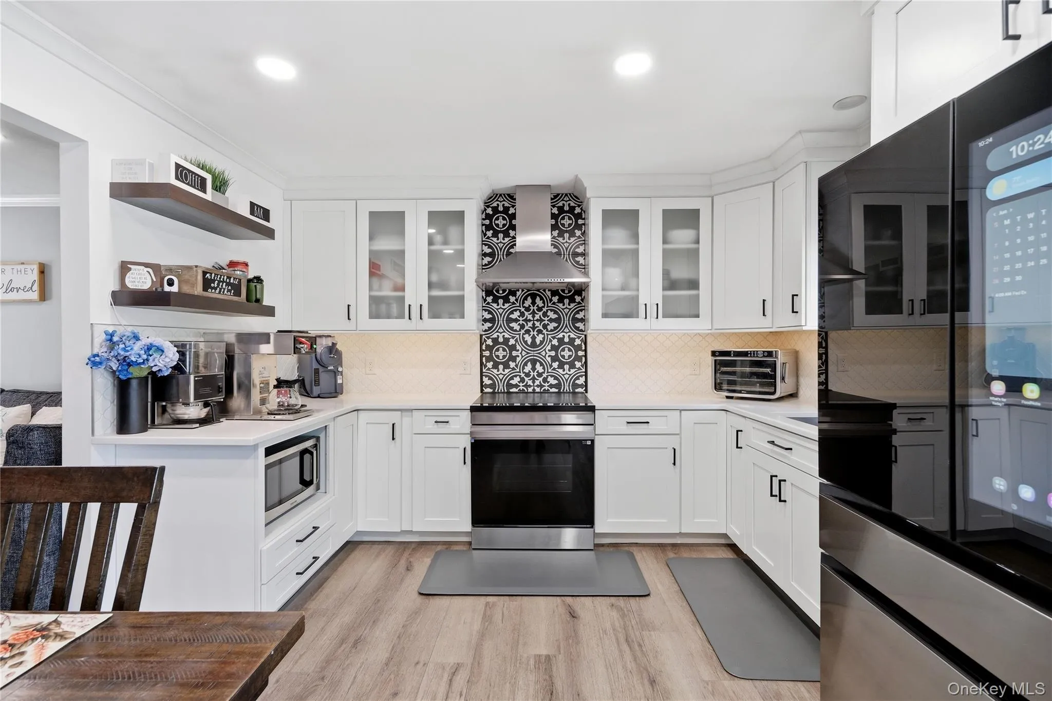 U-shaped kitchen featuring white cabinetry with black hardware, a patterned tile backsplash, stainless steel appliances, recessed lighting, and wood-finish flooring U-shaped kitchen featuring white cabinetry with black hardware, a patterned tile backsplash, stainless steel appliances, recessed lighting, and wood-finish flooring