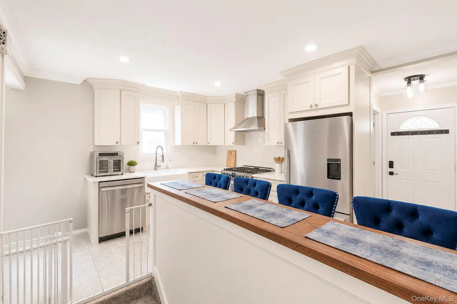 Modern kitchen featuring white cabinetry, stainless steel appliances, recessed lighting, a built-in oven hood, and a light-toned tile floor Modern kitchen featuring white cabinetry, stainless steel appliances, recessed lighting, a built-in oven hood, and a light-toned tile floor