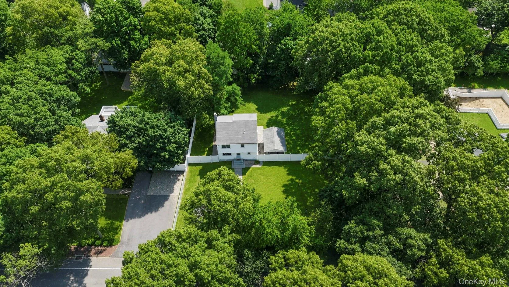 Aerial perspective showcasing a property surrounded by mature trees, featuring a white exterior, a gabled roof, and a verdant lawn Aerial perspective showcasing a property surrounded by mature trees, featuring a white exterior, a gabled roof, and a verdant lawn